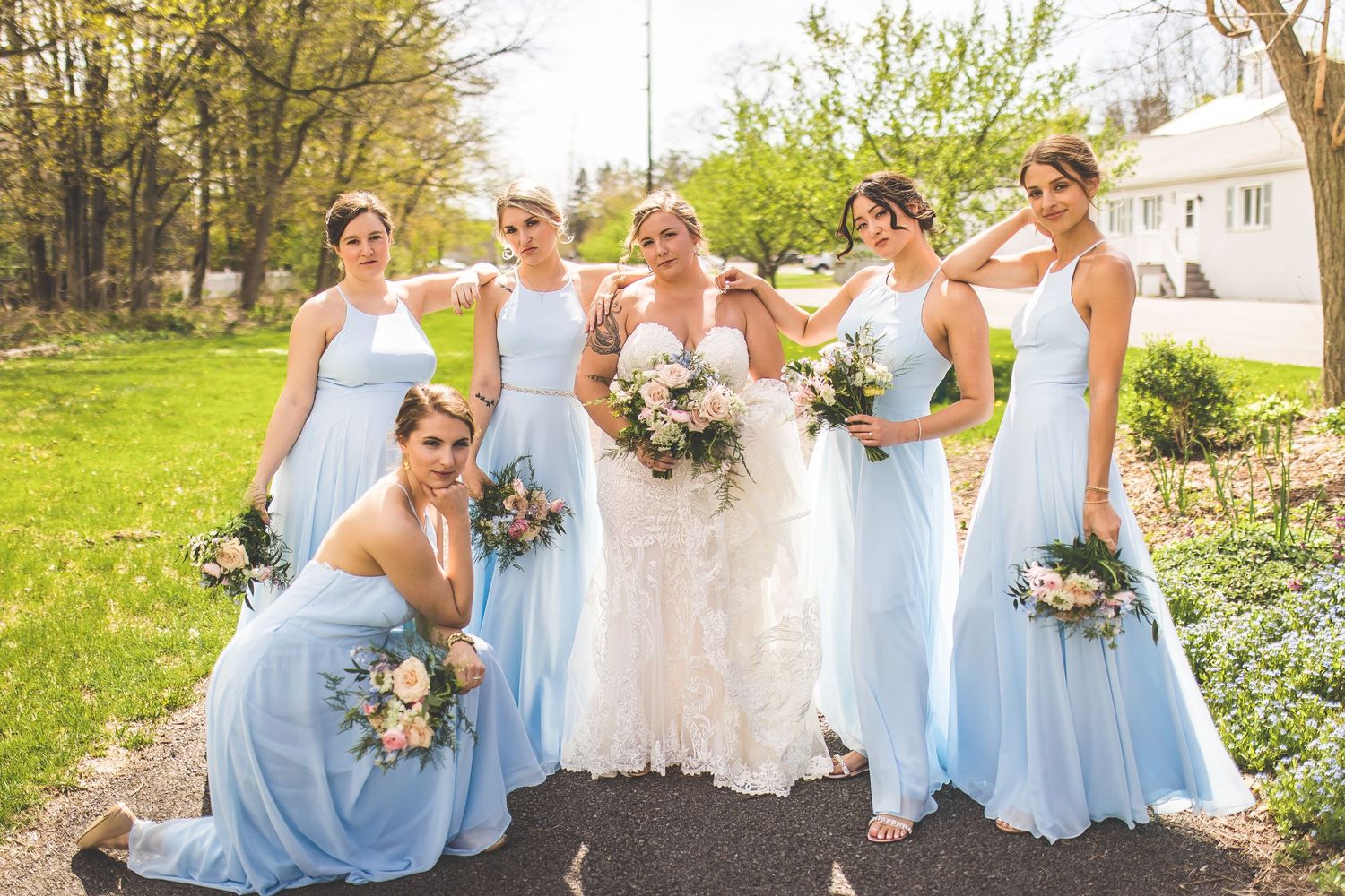 Bridal party in powder blue dresses strikes playful poses on outdoor path.
