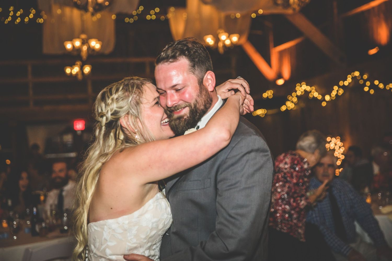 Wedding couple dances beneath twinkling lights at evening reception.