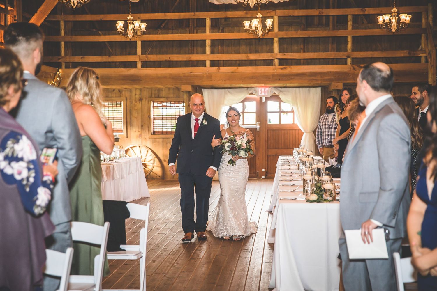 Panoramic view of rustic barn wedding ceremony with guests seated and decorated aisle.