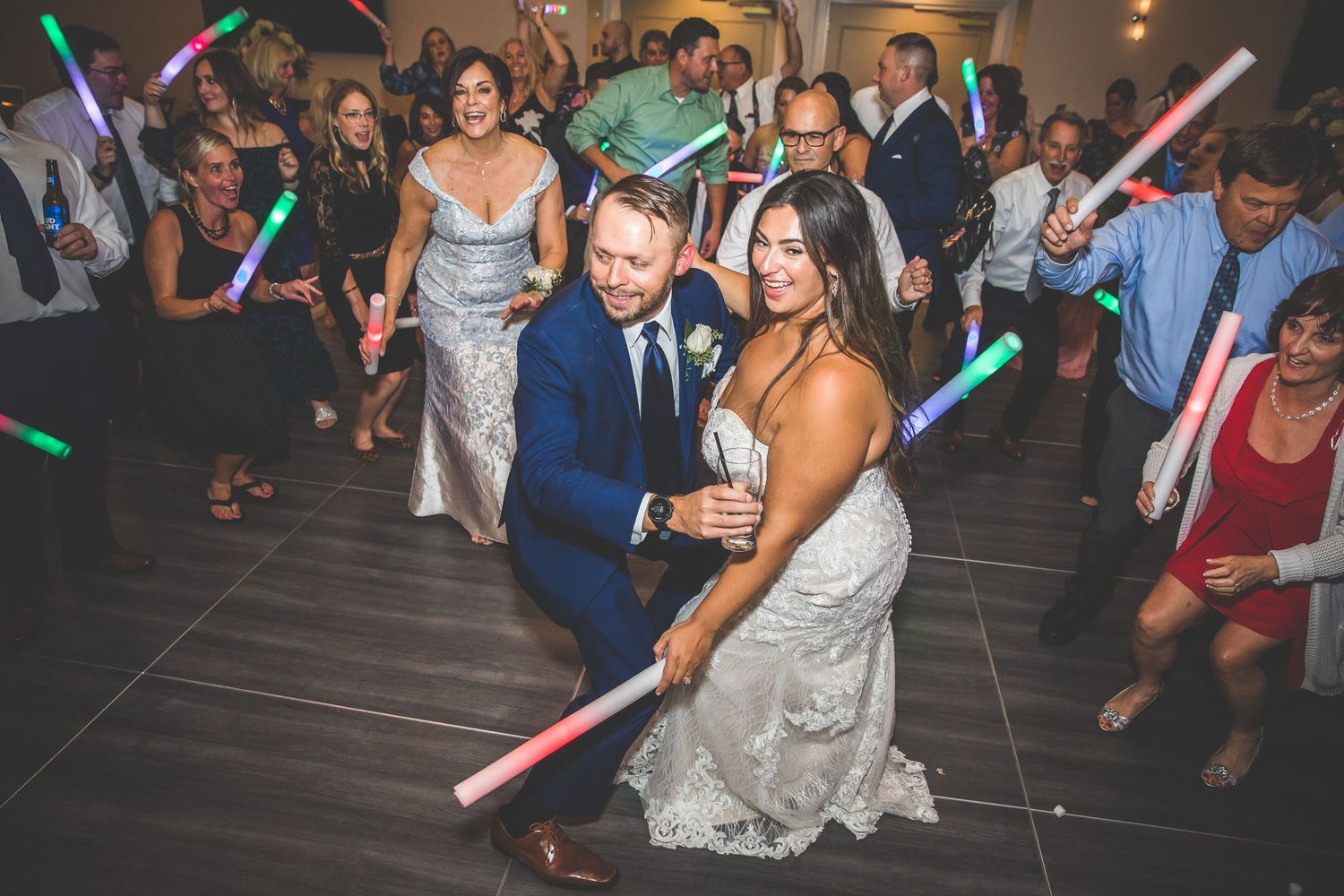 Wedding party dancing with colorful LED glow sticks during an energetic reception celebration.