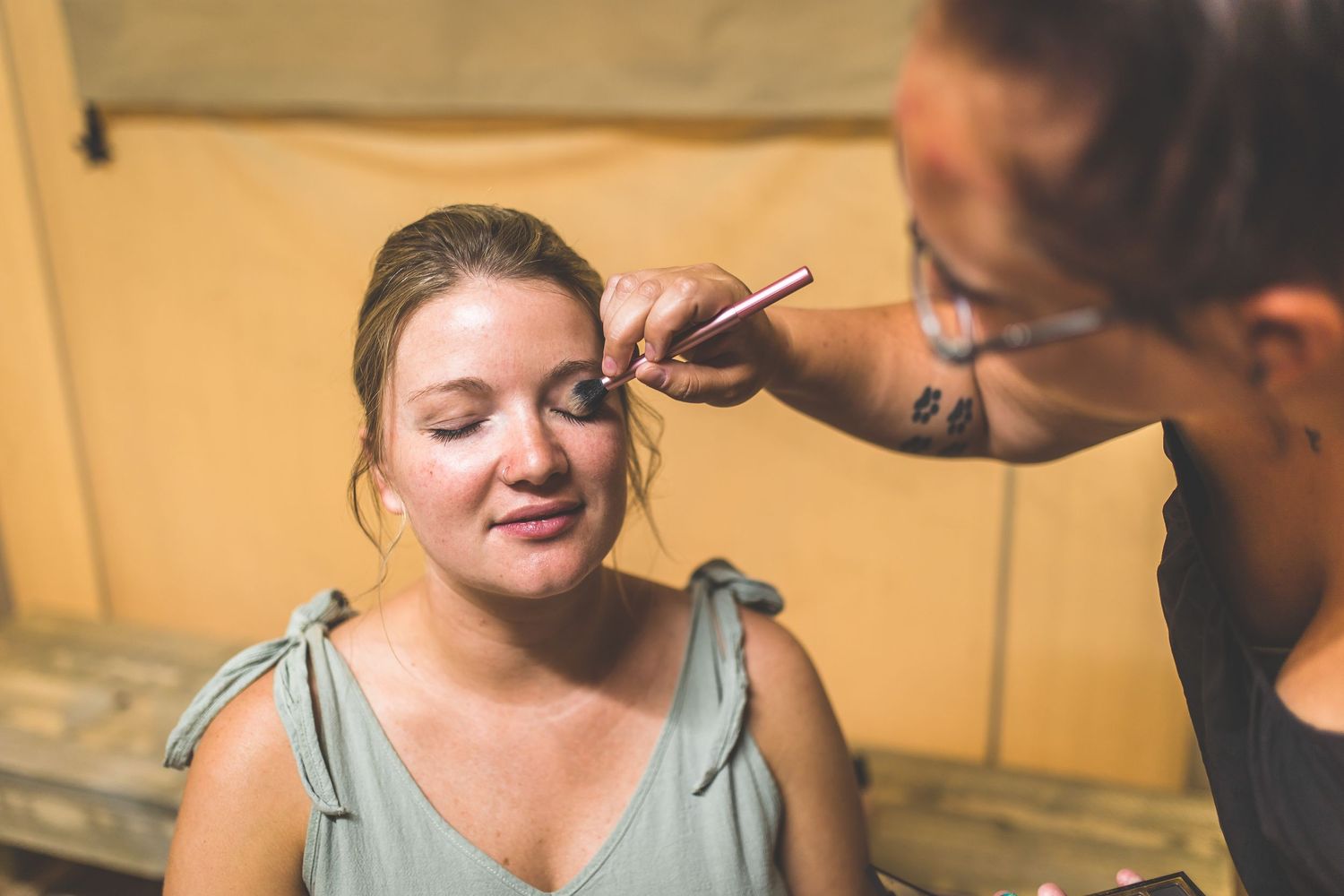 Wedding preparation scene with makeup being applied in natural lighting.
