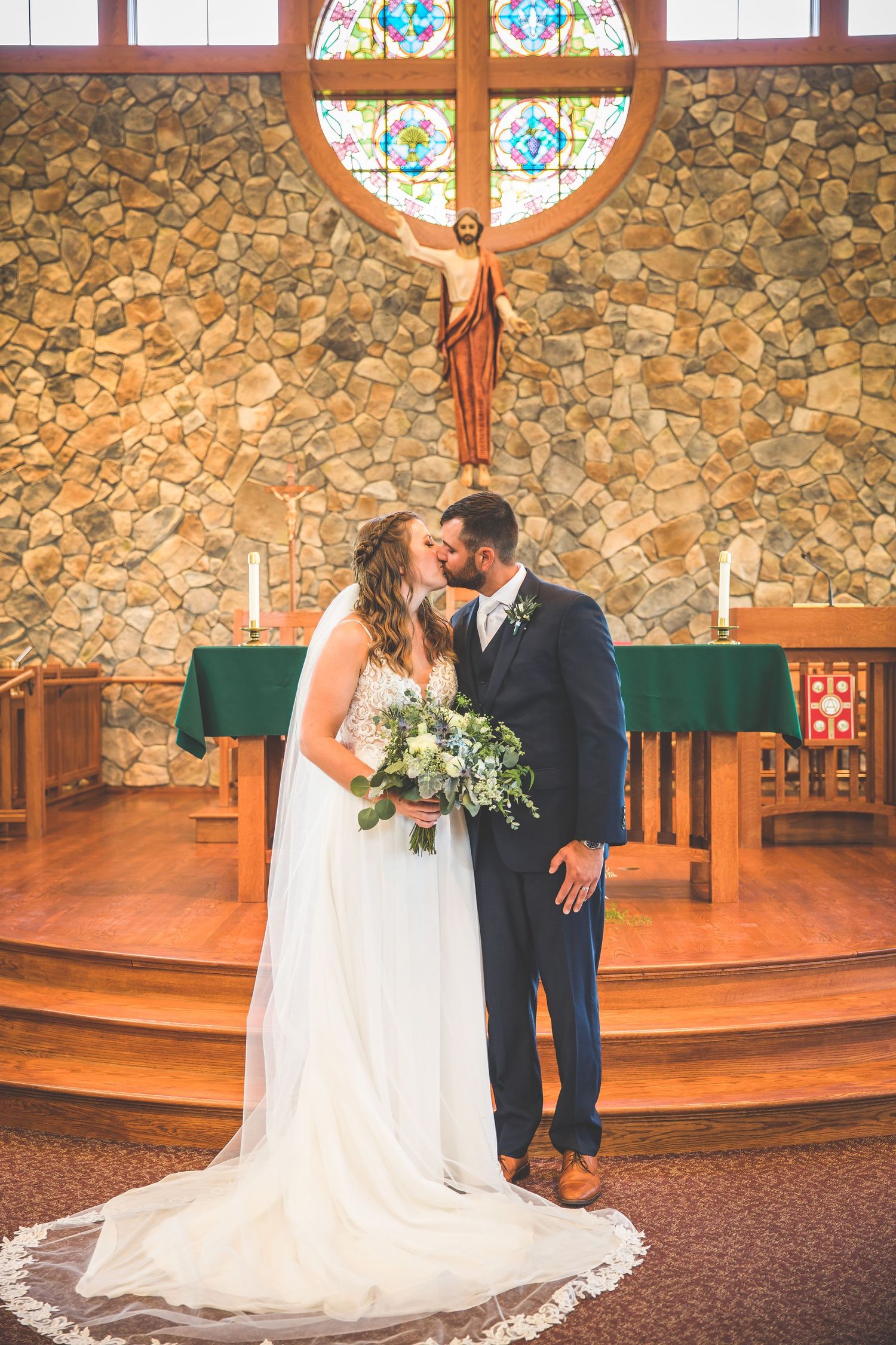 Romantic wedding moment captured in front of a stone wall and stained glass windows.