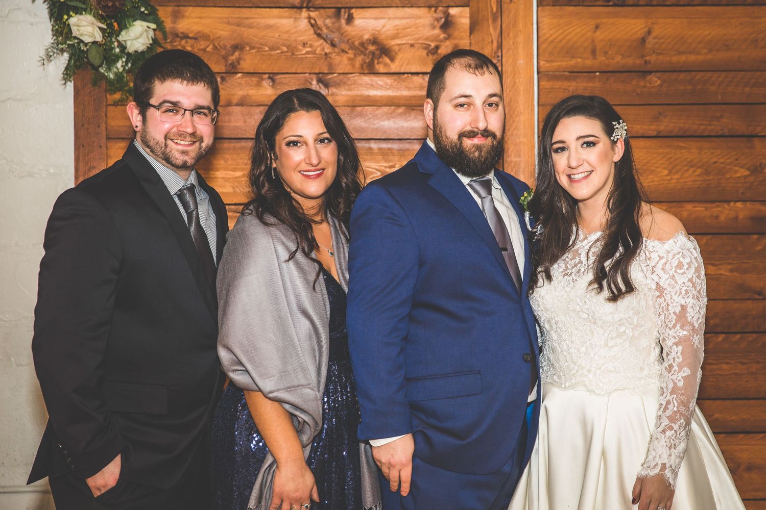 Wedding party poses together against rustic wooden wall backdrop.