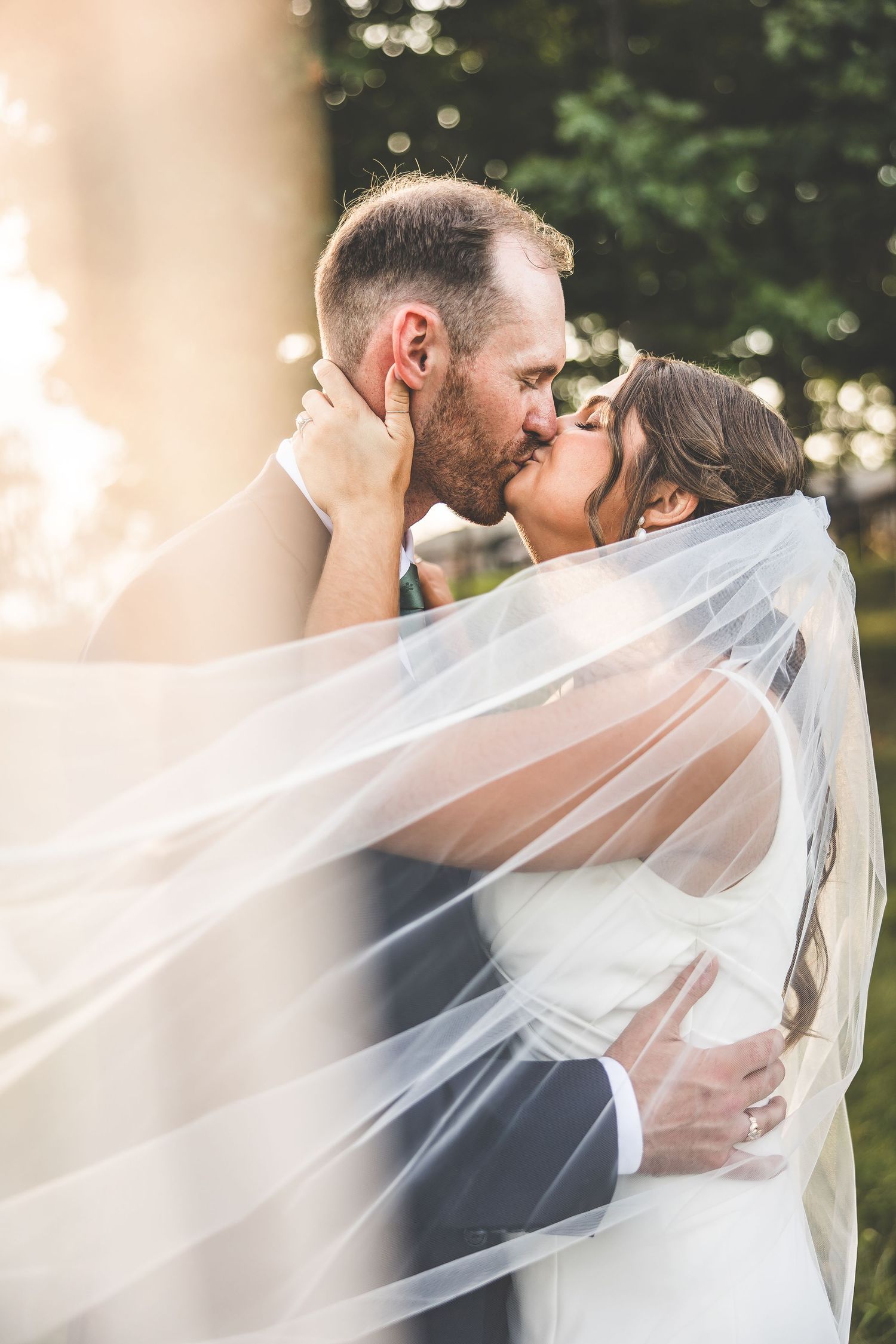 Romantic wedding portrait with flowing veil creating ethereal effect in natural light.