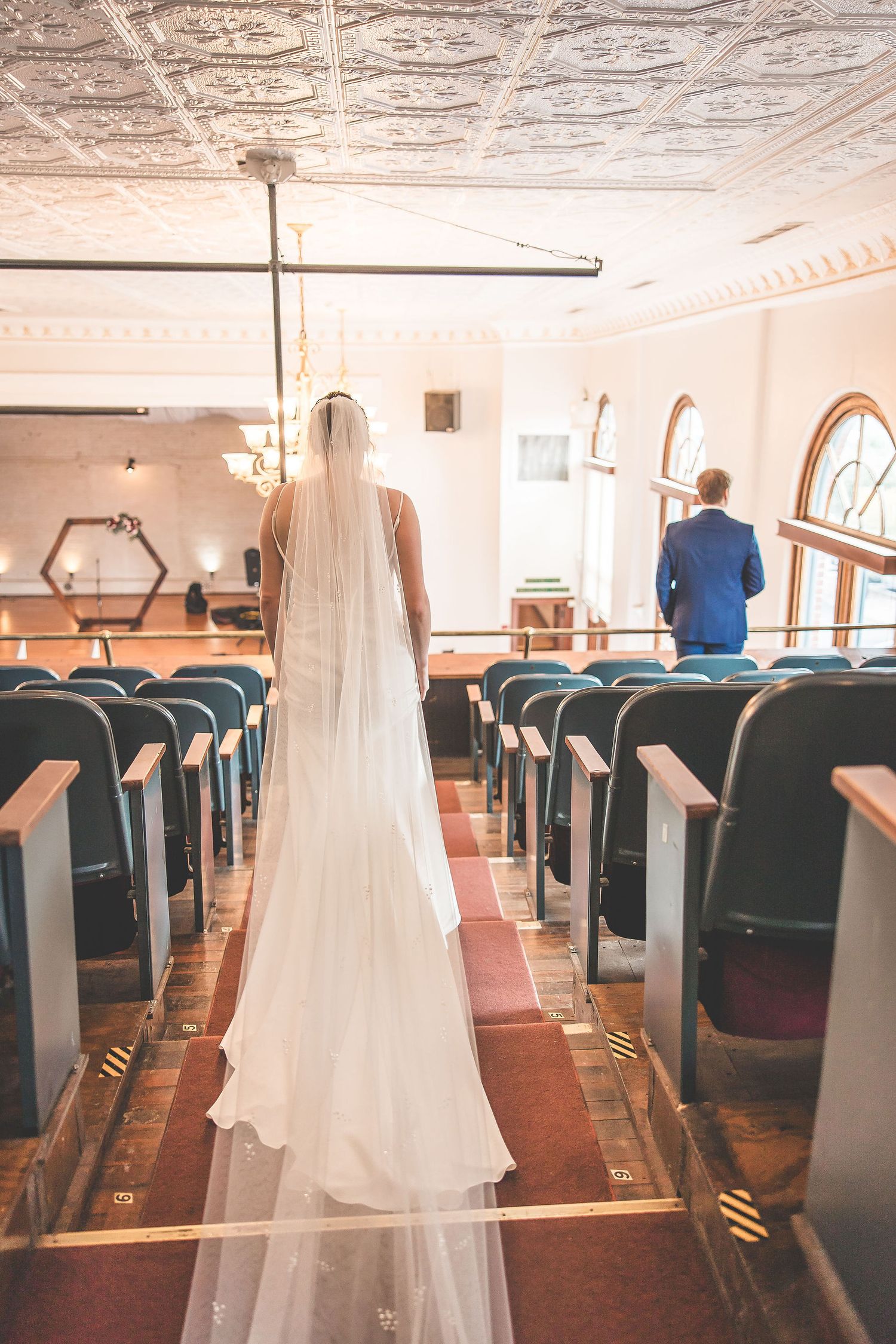 Empty wedding venue with rows of blue chairs and elegant chandeliers hanging from ornate ceiling.