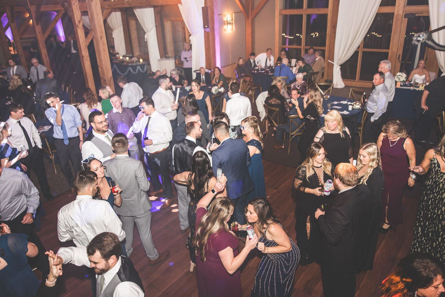 Wide shot of a packed dance floor with guests celebrating under purple ambient lighting.