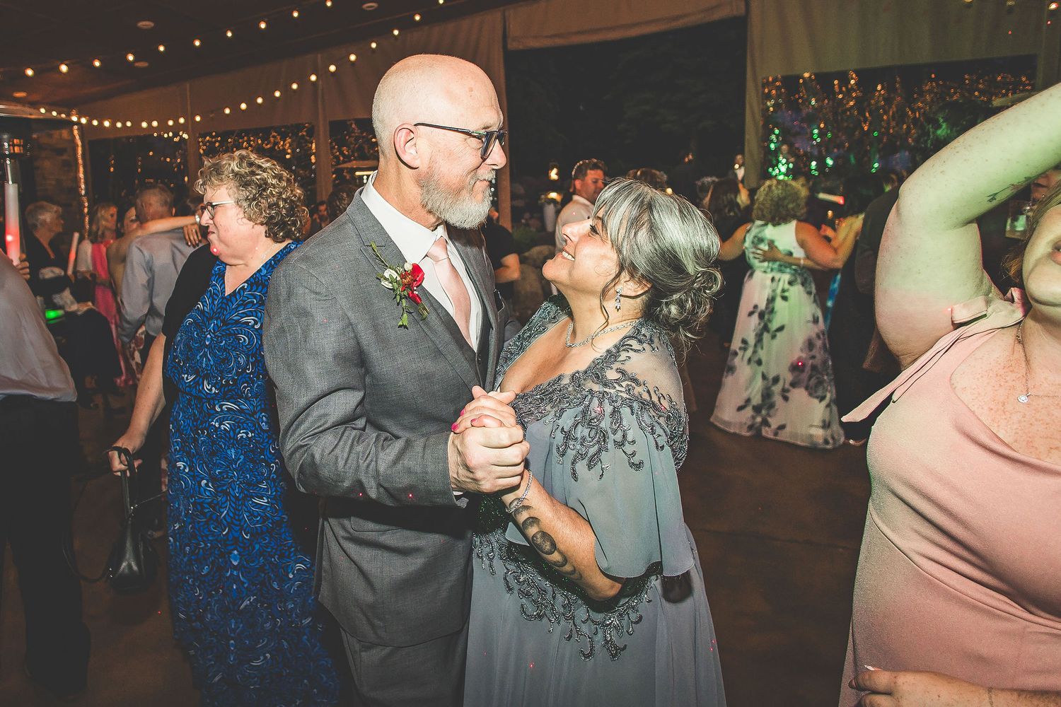 Couples slow dancing at an elegant wedding reception with string lights overhead.