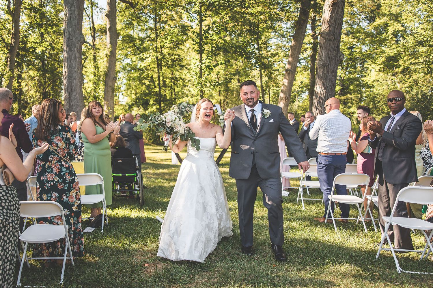 Wedding ceremony setup in a wooded grove with guests mingling before the event.