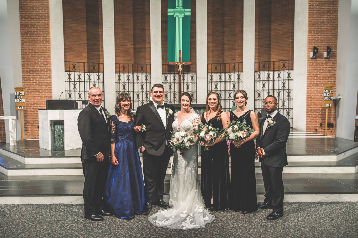 Formal wedding group photo taken in front of traditional brick church architecture.