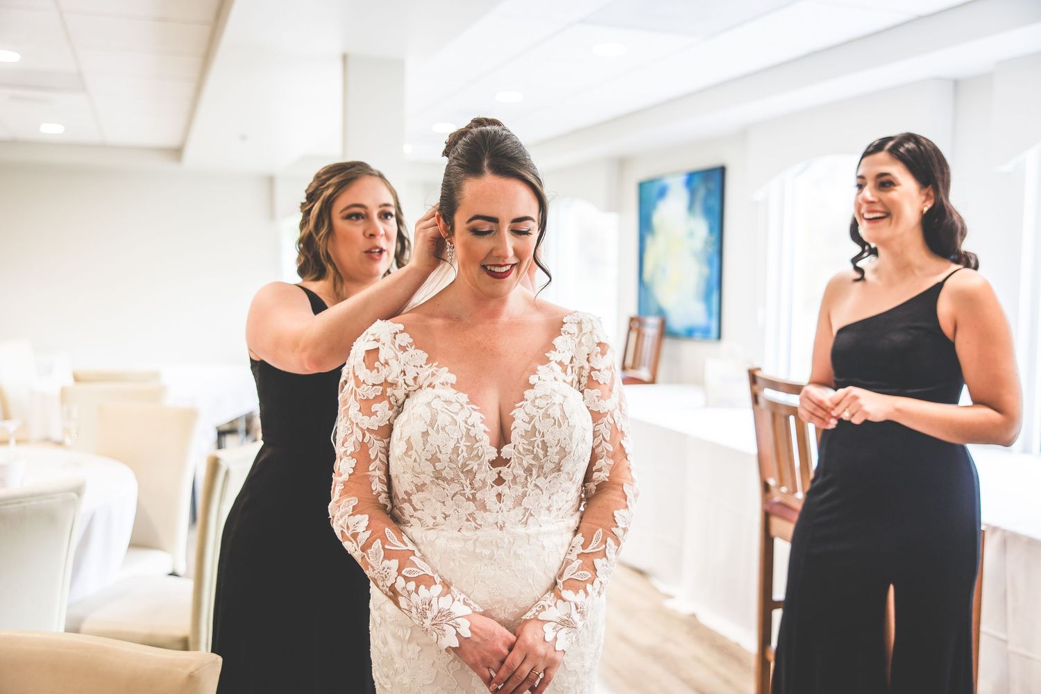 Wedding party helps bride get ready in bright indoor space.