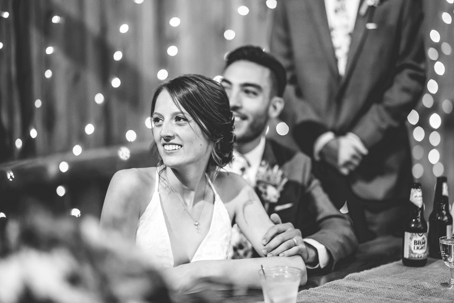 Wedding guests celebrate during reception in rustic barn venue with twinkling lights overhead.