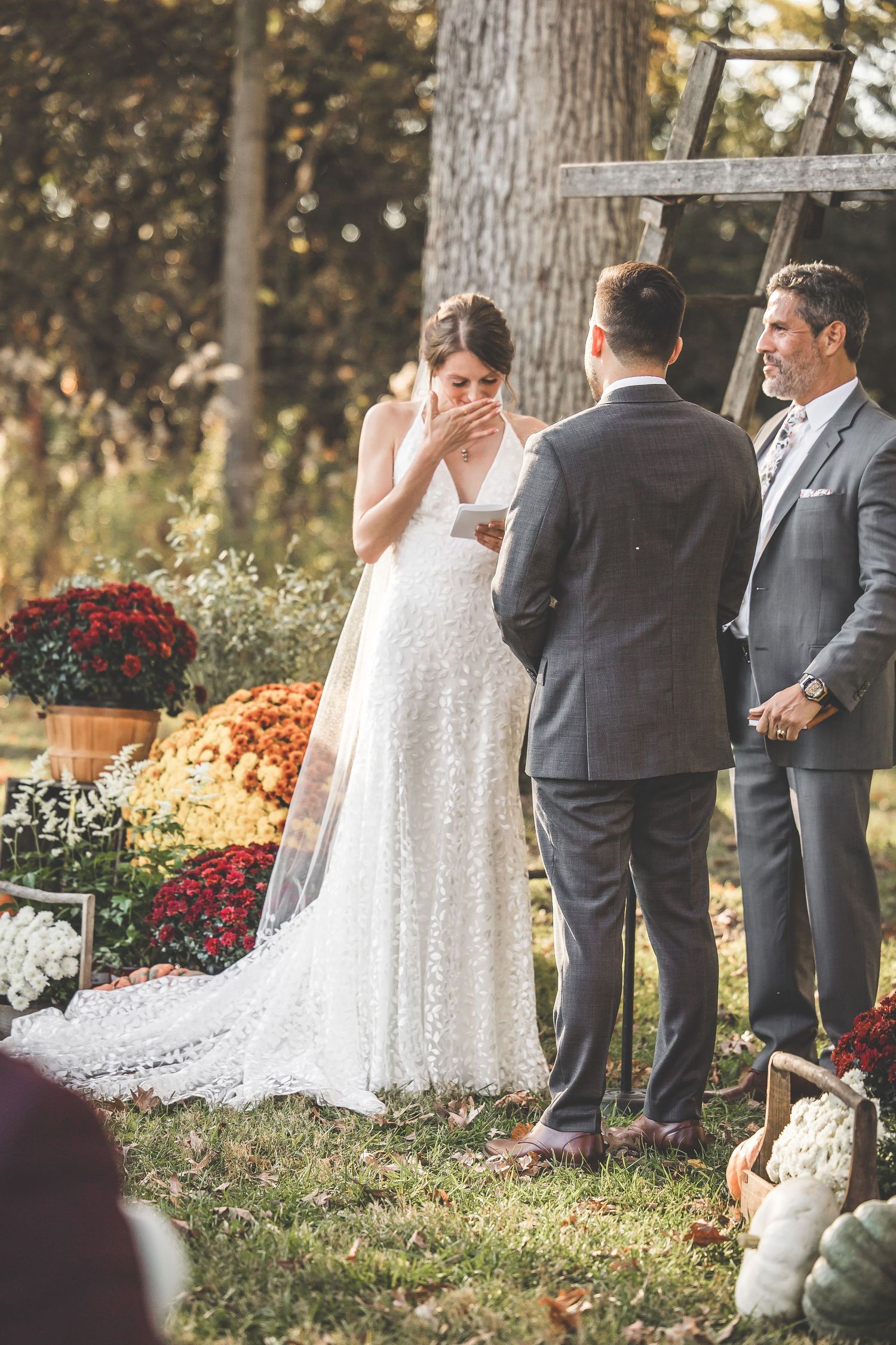 Emotional wedding ceremony moment under wooden arch decorated with fall mums and pumpkins.