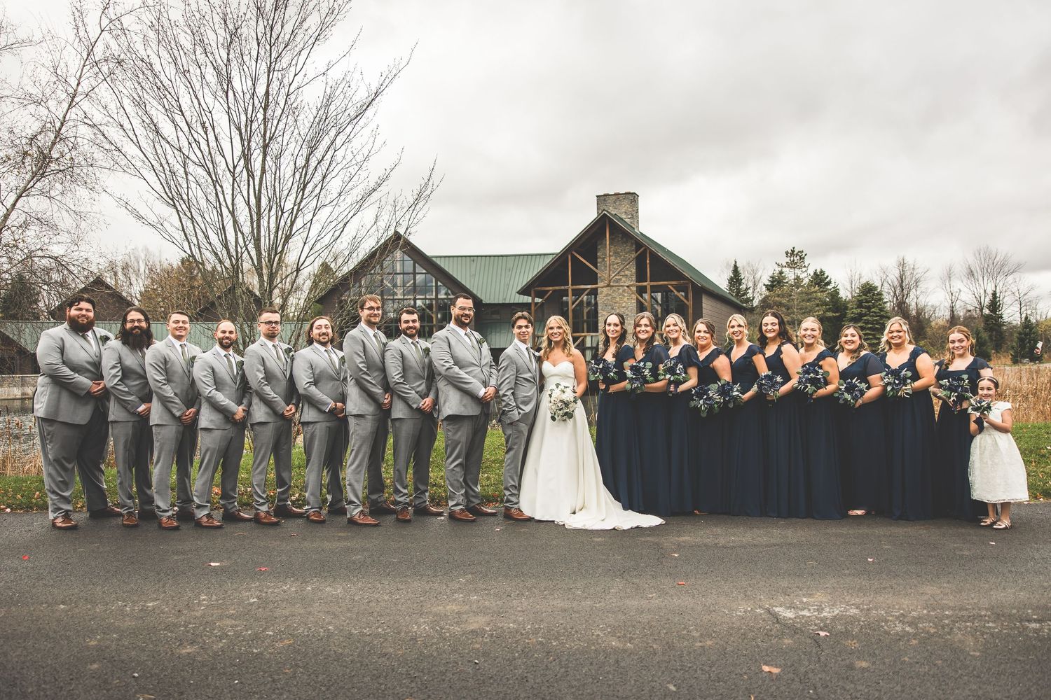 Large wedding party lined up for formal photos against autumn backdrop.