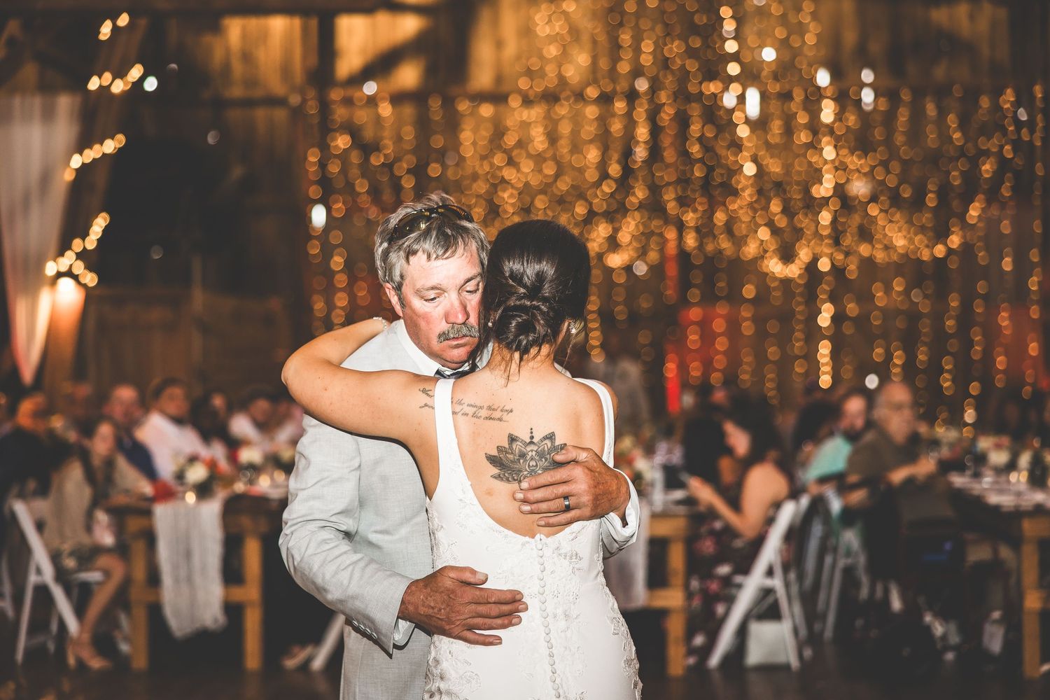 An intimate slow dance moment during a barn wedding reception with glowing lights in the background.