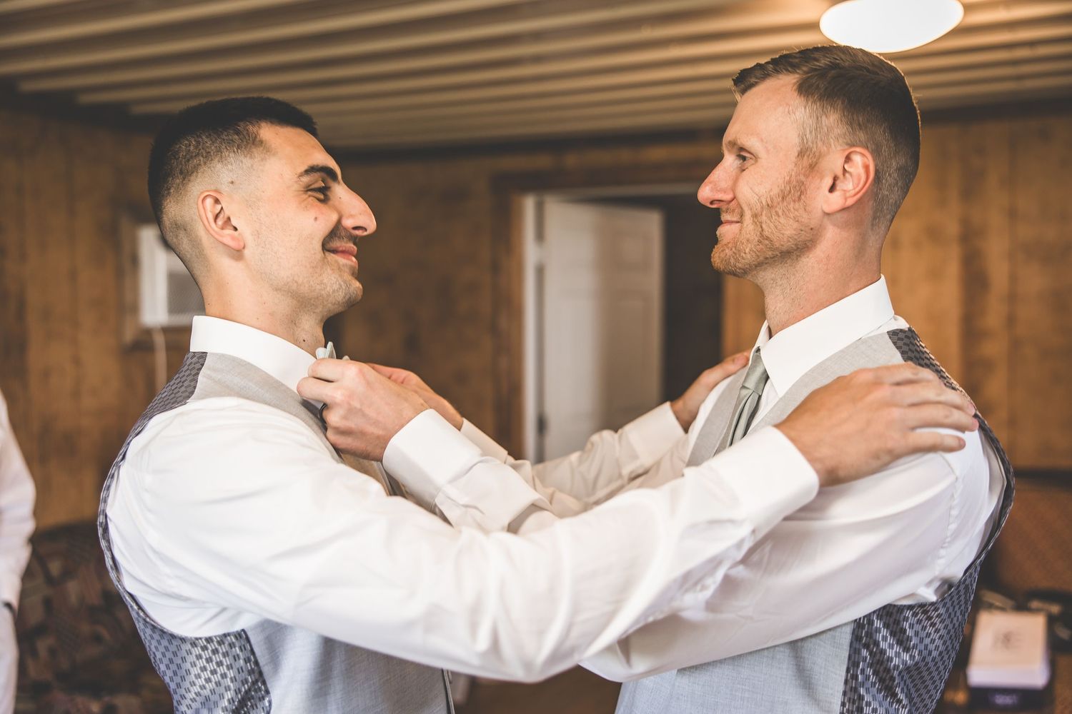 Groomsmen in white shirts helping each other with formal attire.