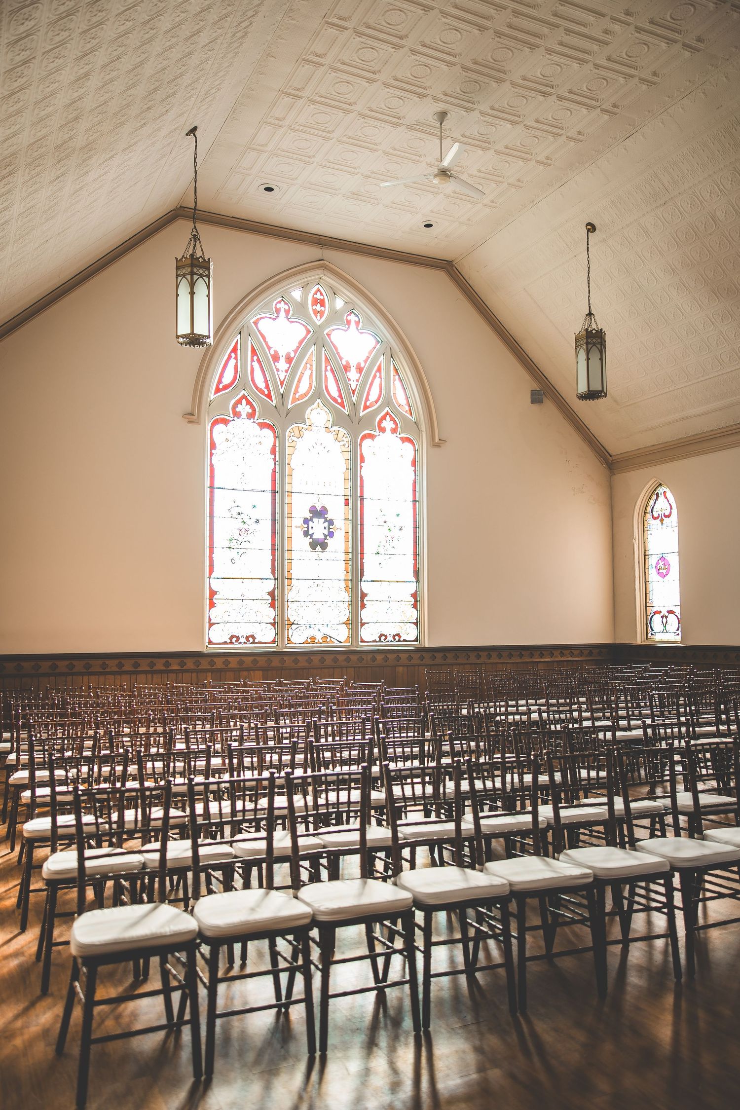 Empty church ceremony space with rows of dark chairs and stained glass windows.