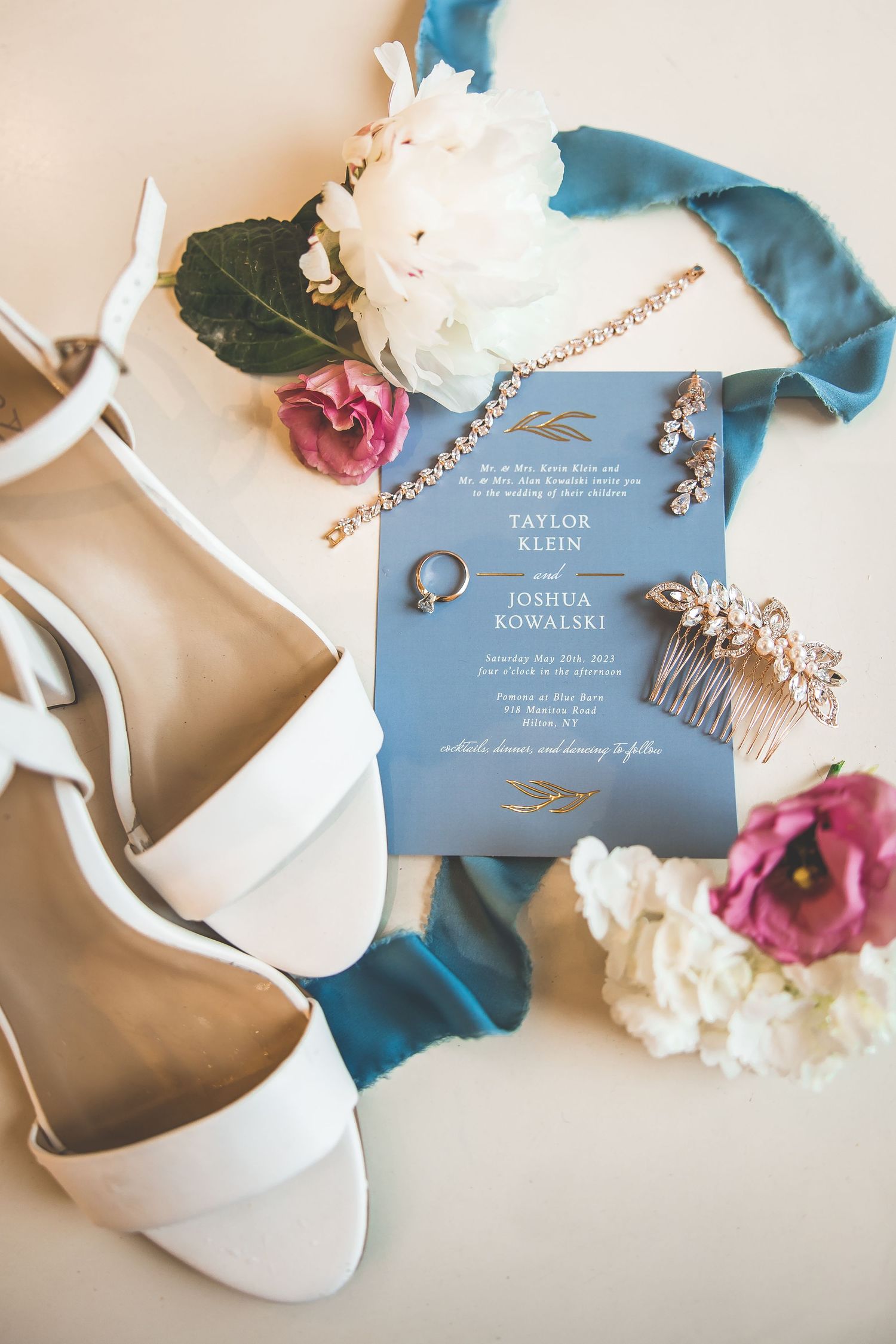 Wedding details with blue invitations, white shoes, and floral accents on beige background.
