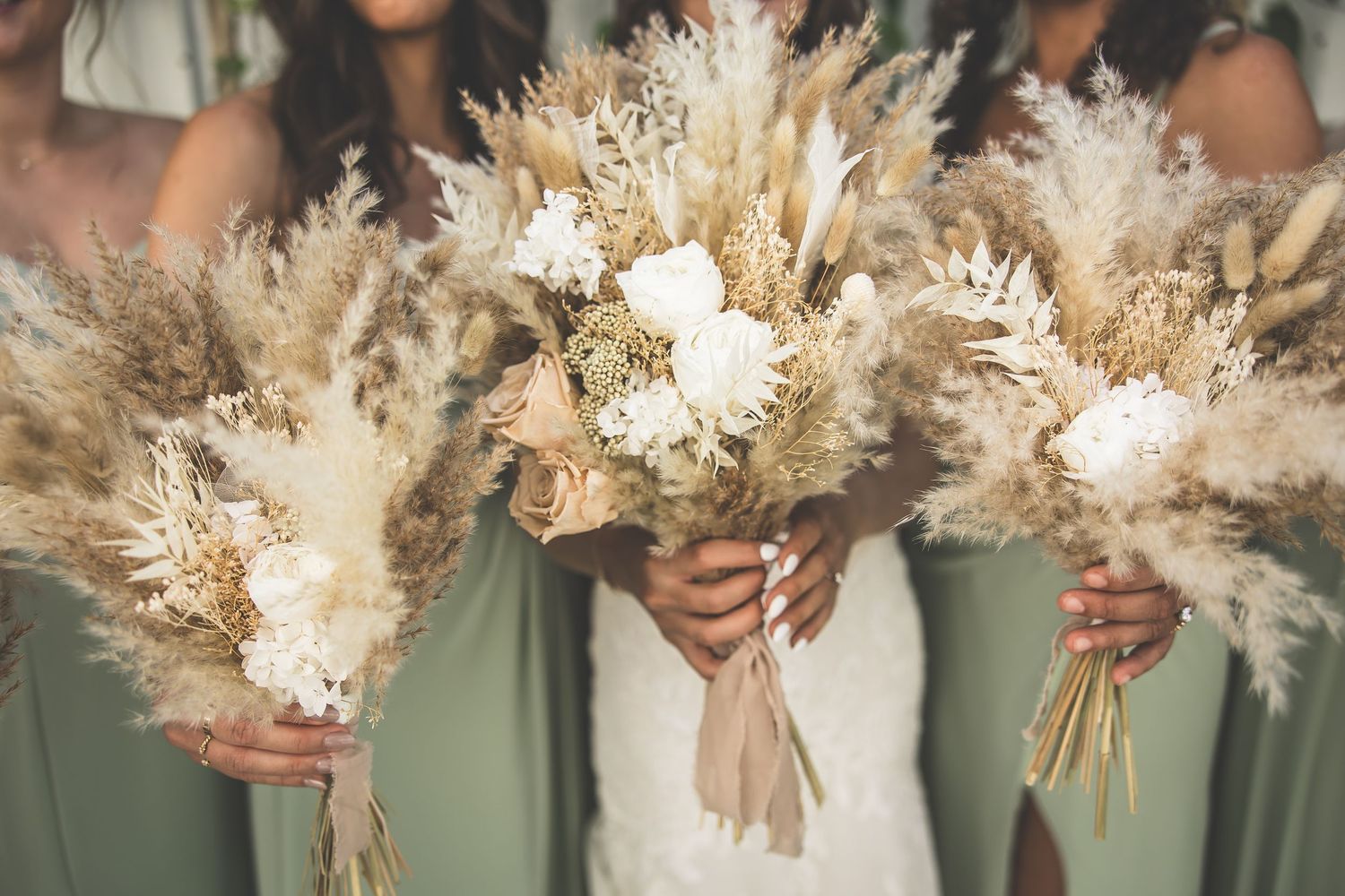 Elegant bouquets of dried pampas grass and white flowers held against sage green dresses.