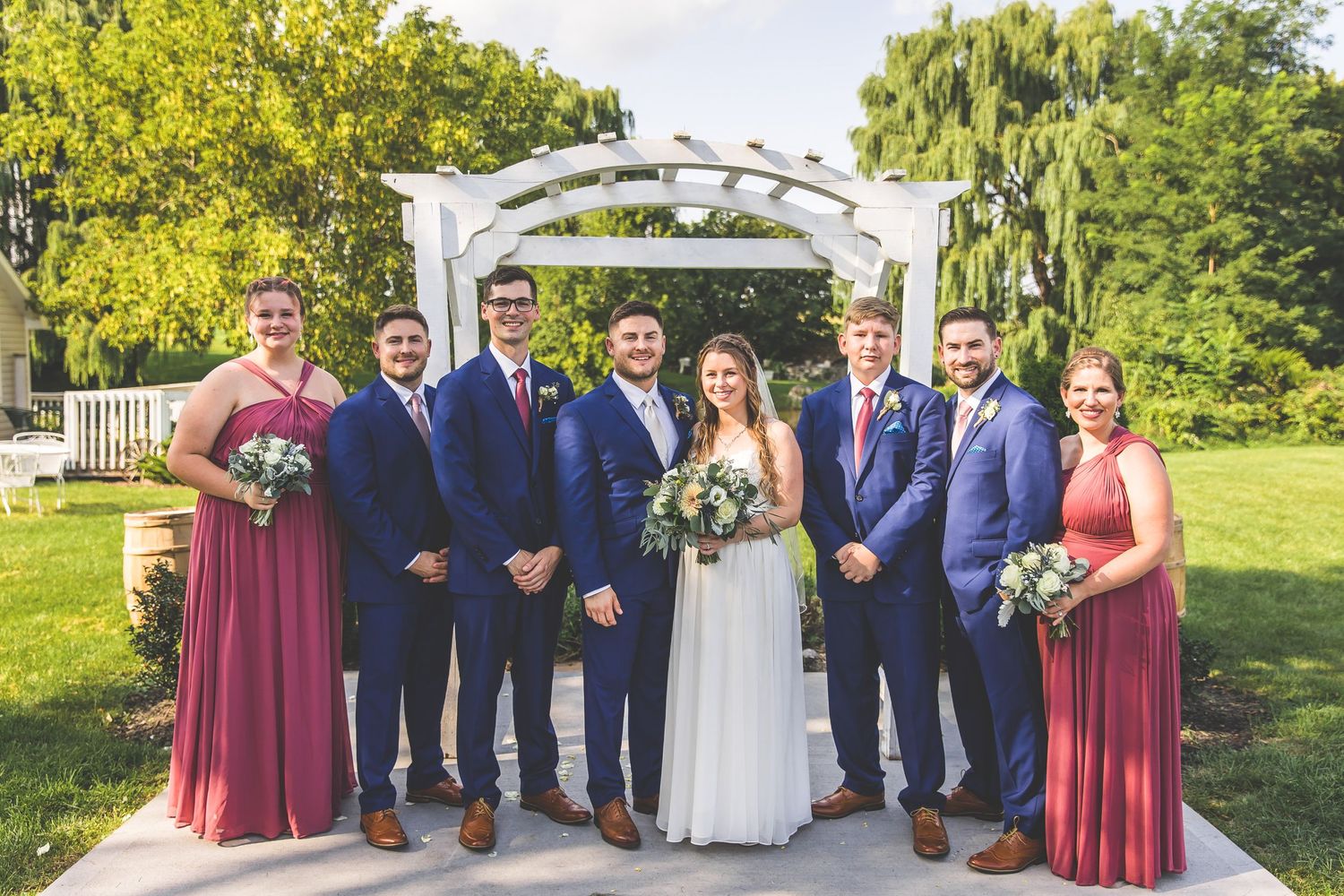 Complete wedding party portrait showcasing burgundy bridesmaids dresses and navy groomsmen suits.