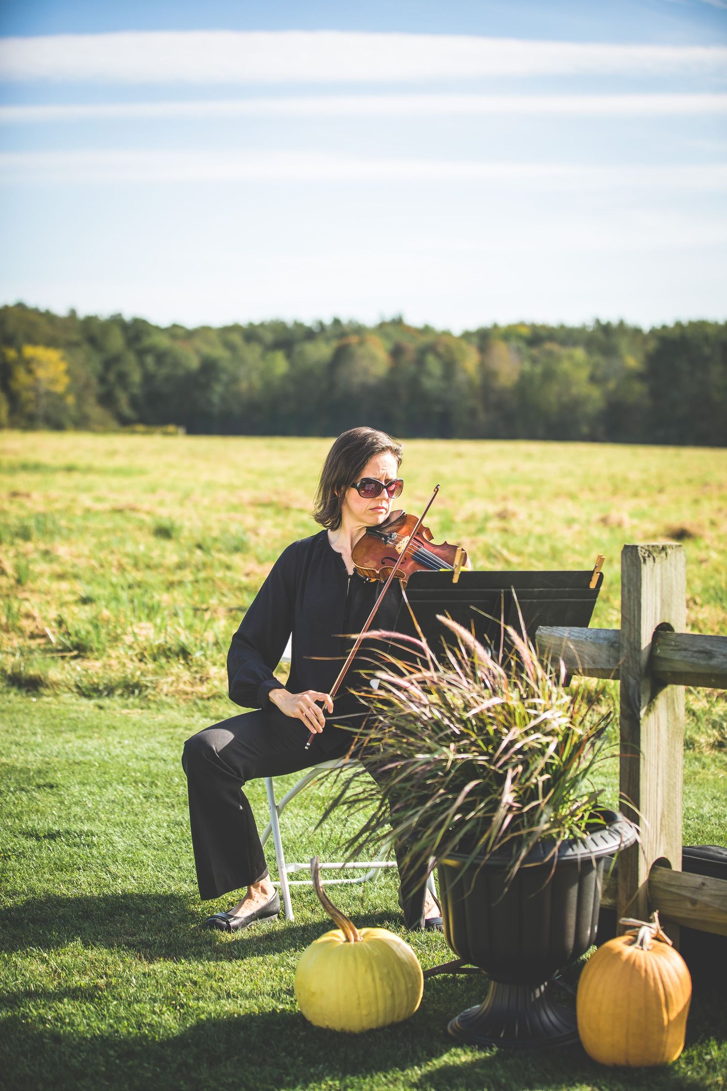 Violinist performs outdoors next to fall pumpkins in a garden setting.