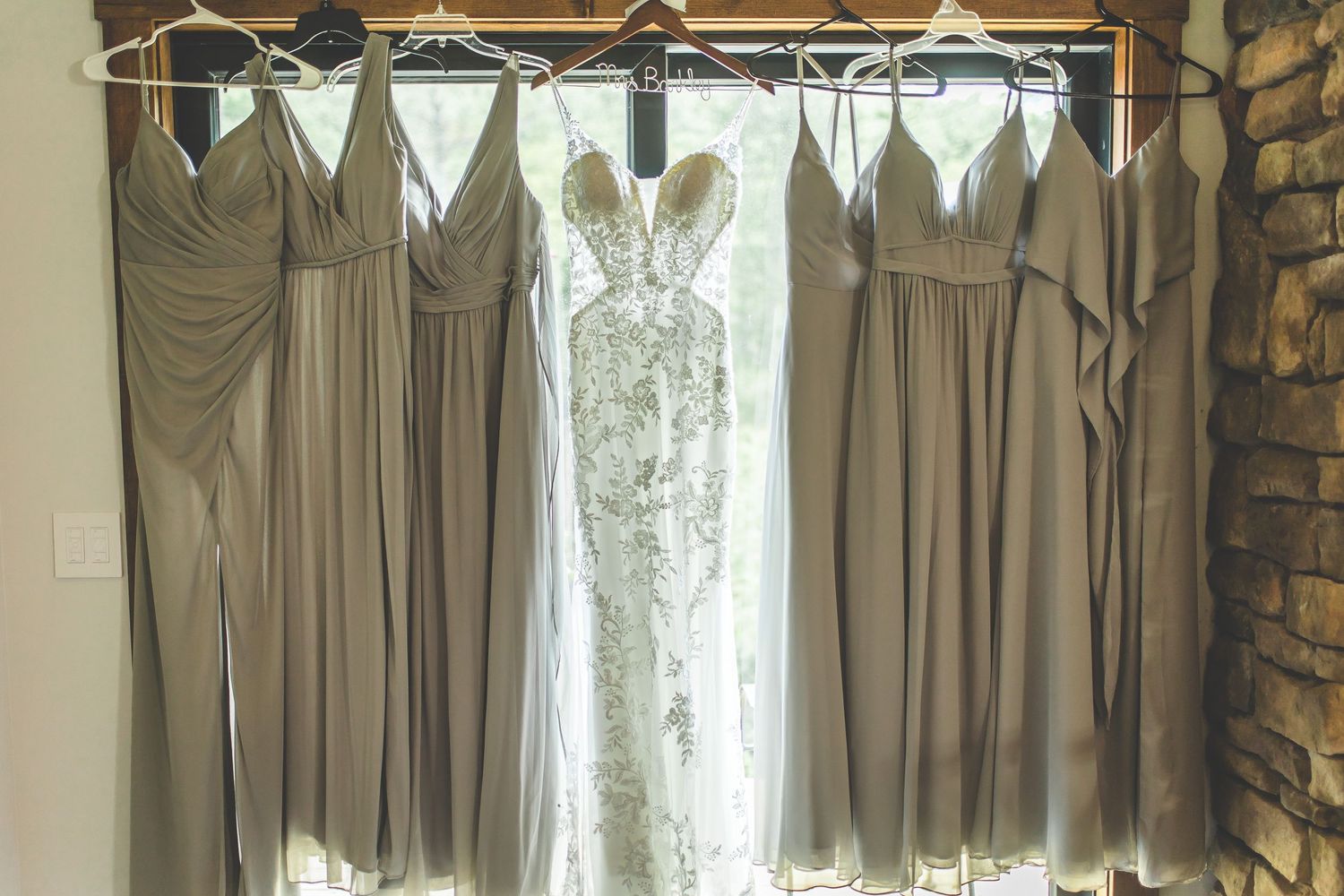Row of gray bridesmaid dresses hanging on wooden hangers against a neutral wall.