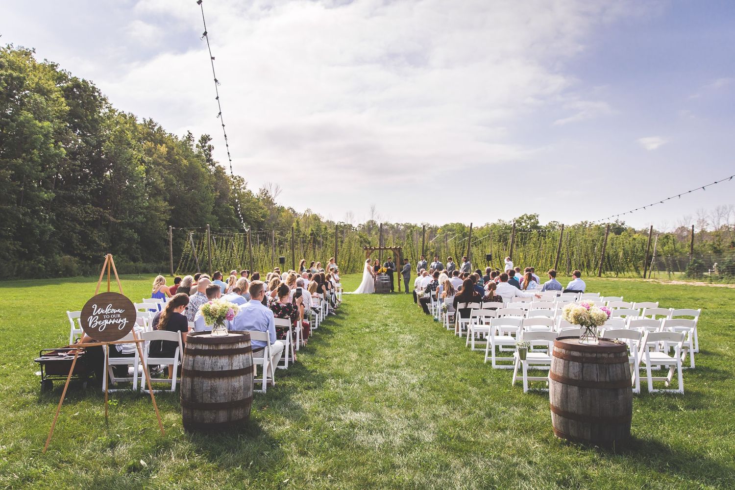 Panoramic view of outdoor wedding ceremony setup with white chairs and wooden arch.