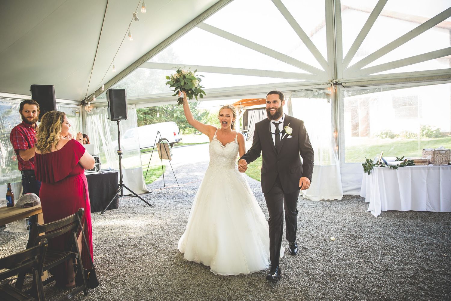 Wedding reception setup under white tent with tables and rustic decor.