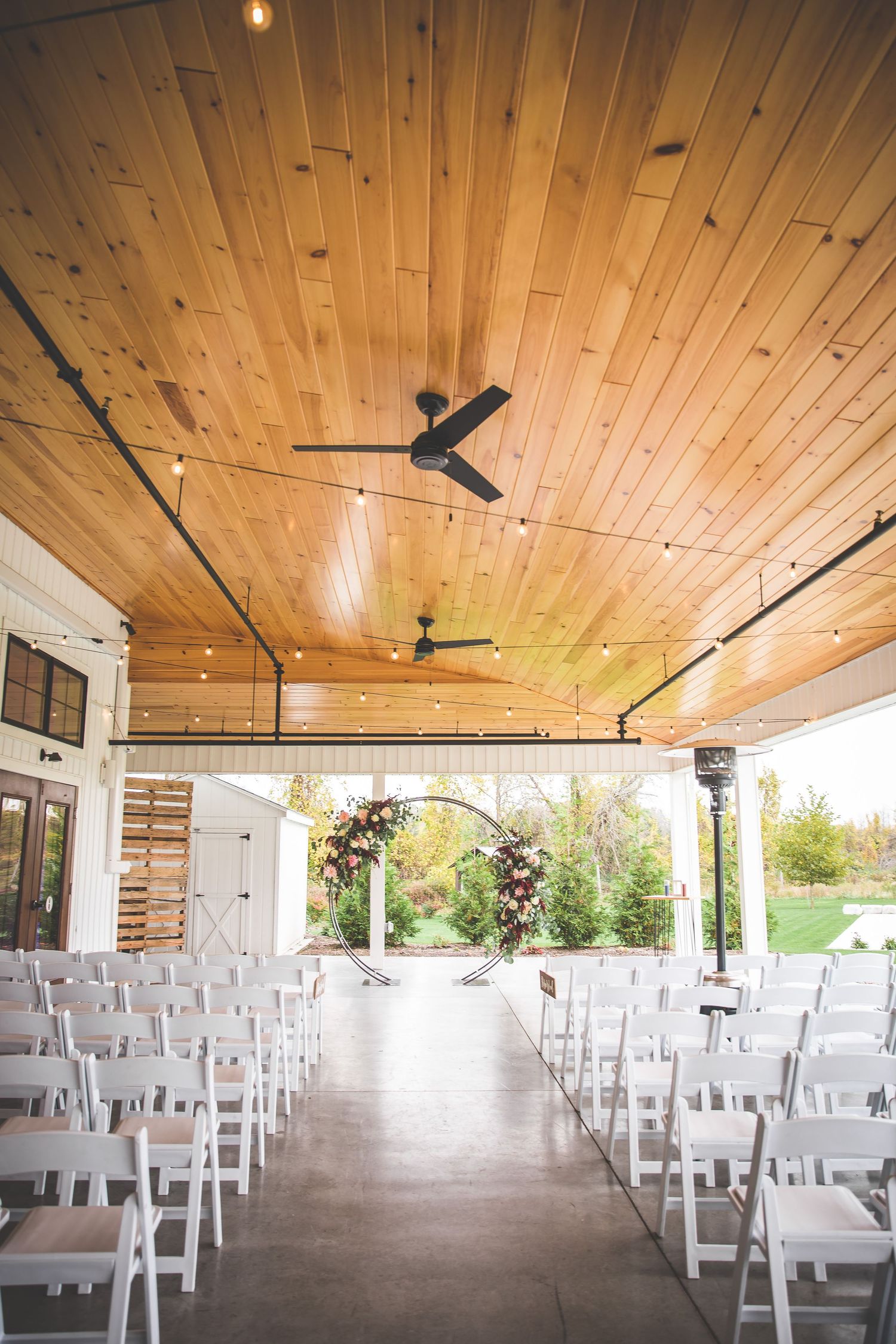 Wedding venue interior with wooden ceiling, white chairs, and natural lighting.
