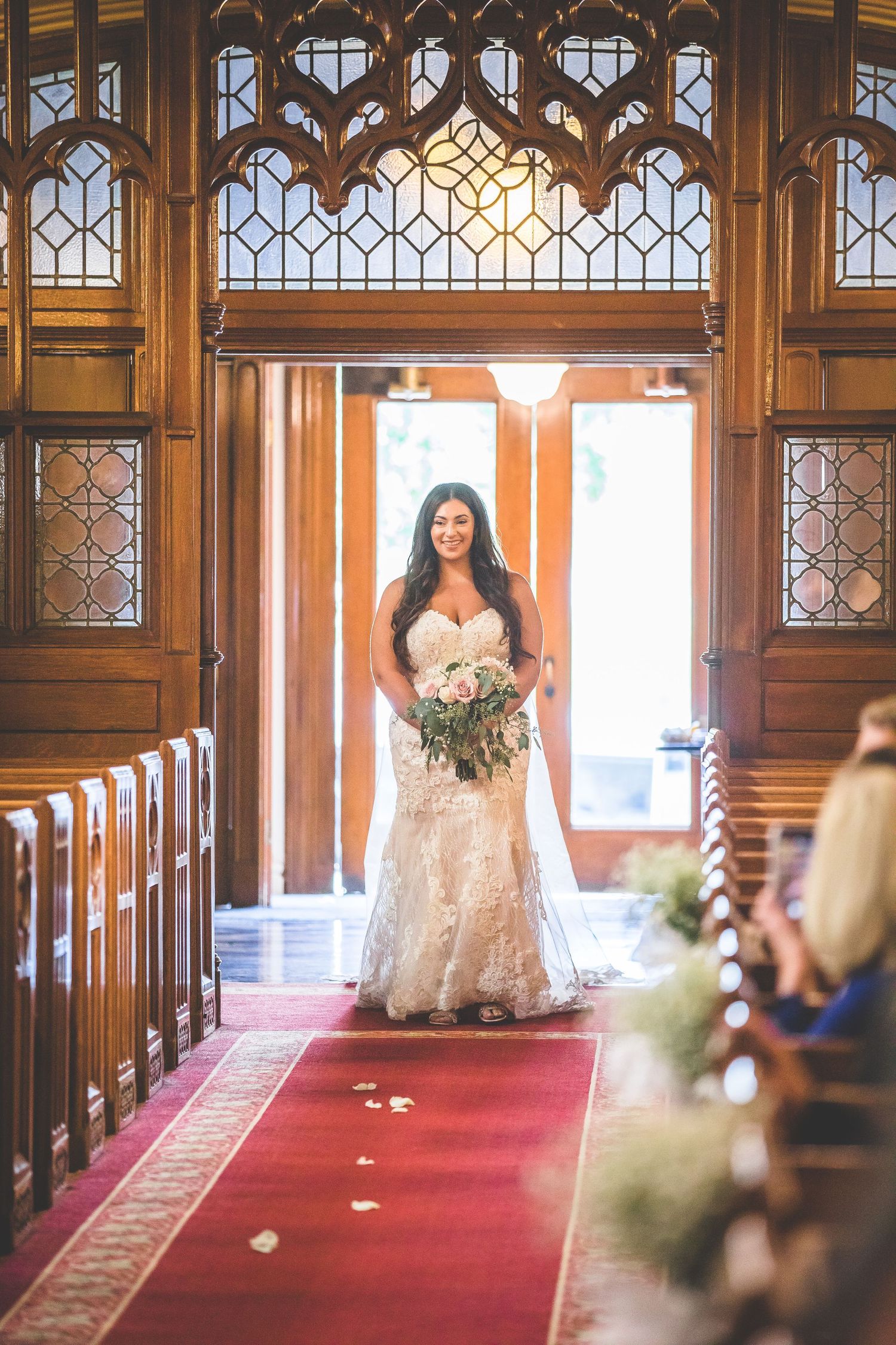 Bride walking down ornate church aisle with gothic architecture and red carpet.