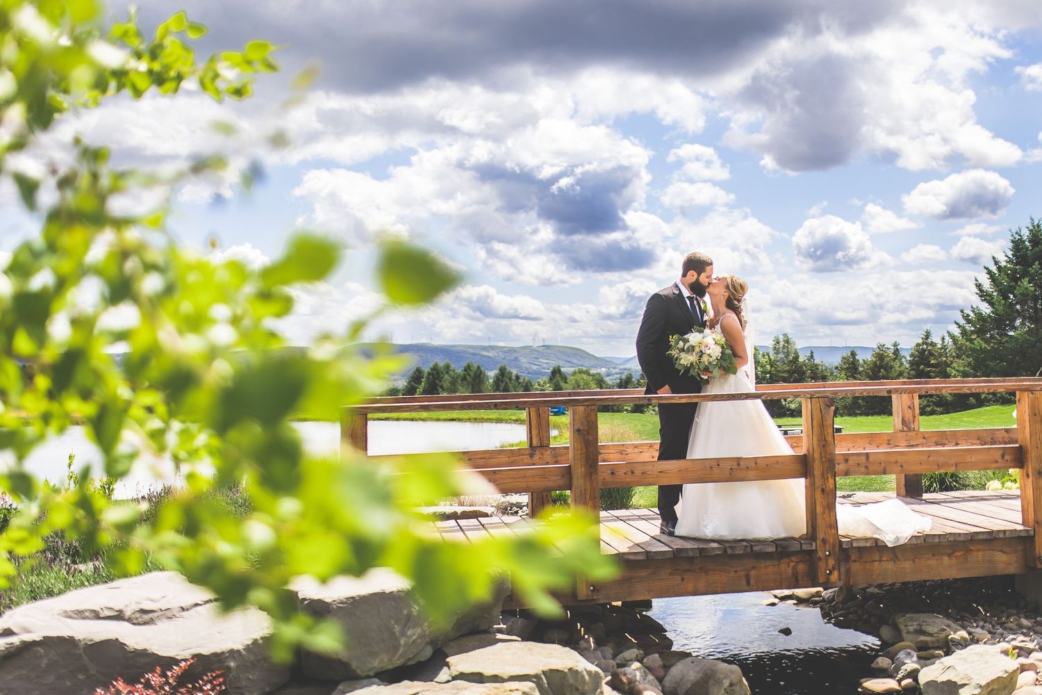 Dreamy wedding portrait on wooden bridge with soft focus foliage and clouds.