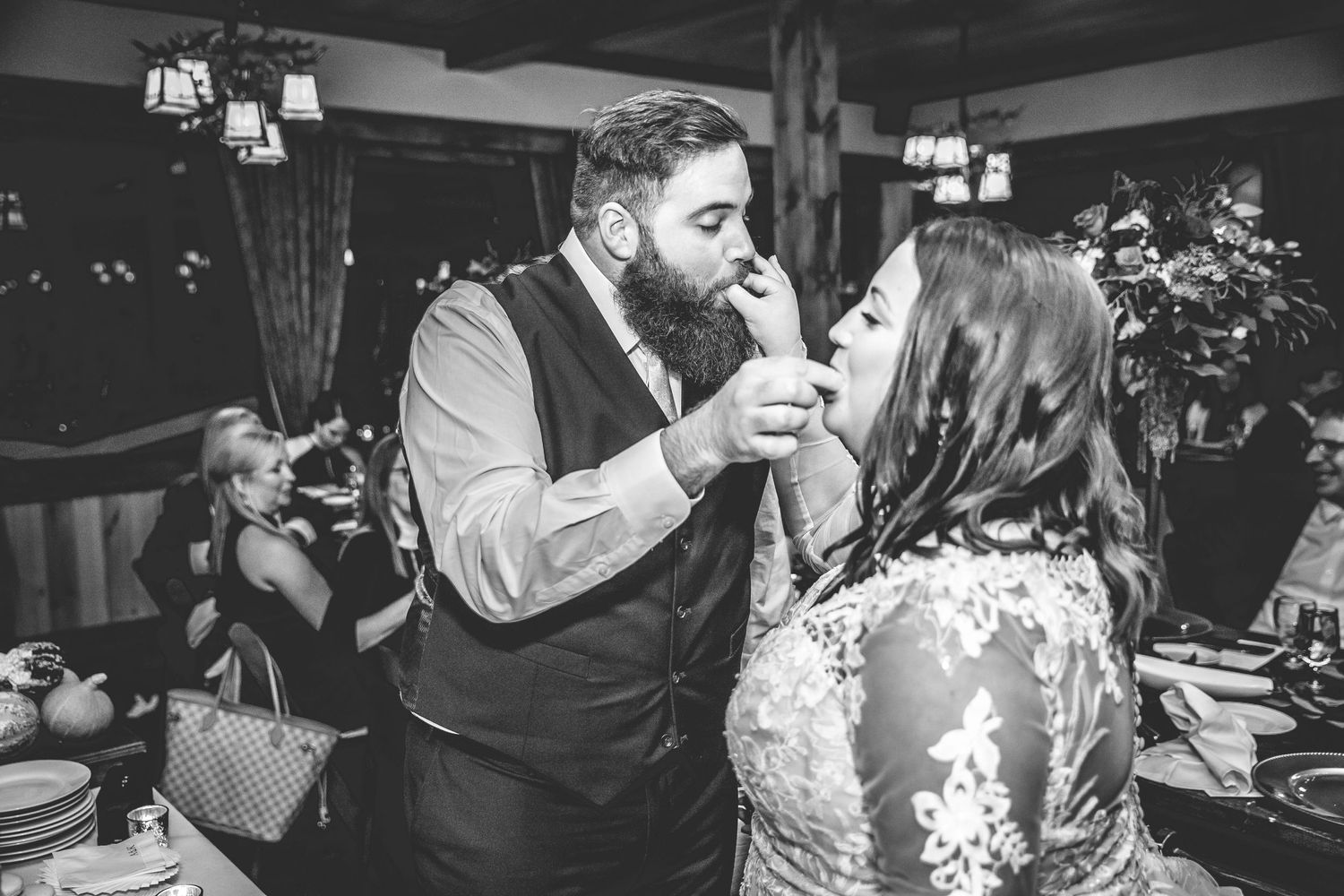 Black and white photo of wedding guests celebrating at reception with dim lighting and rustic decor.