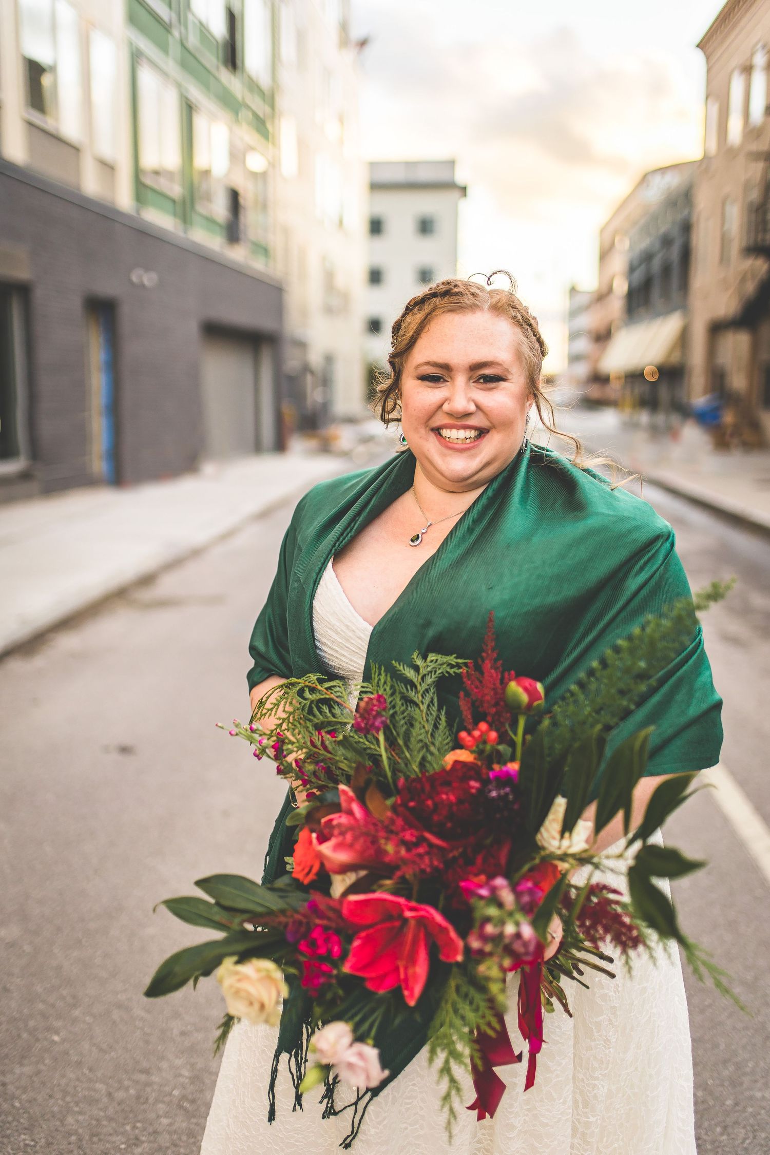 Elegant wedding bouquet featuring vibrant red flowers and greenery against a white dress.
