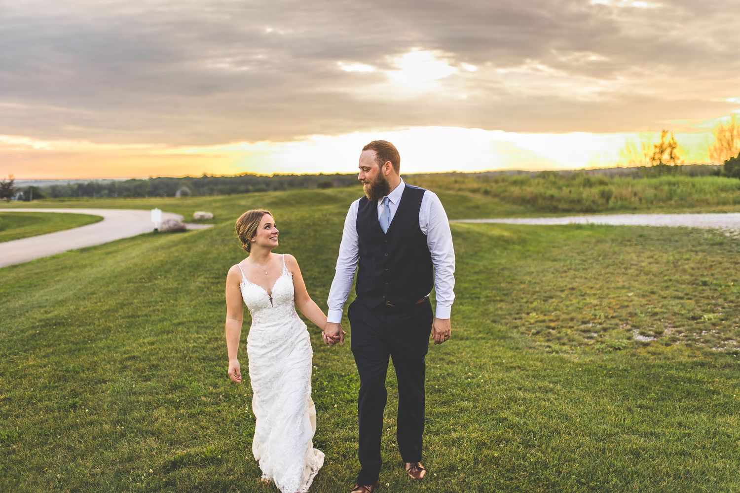 Bride and groom stroll together across a scenic hilltop at dusk.