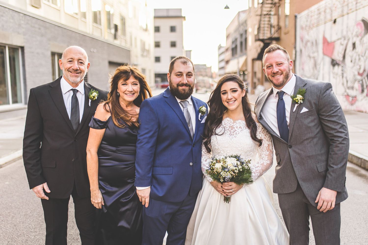 Bridal party gathers for casual portrait on city street with vintage architecture.
