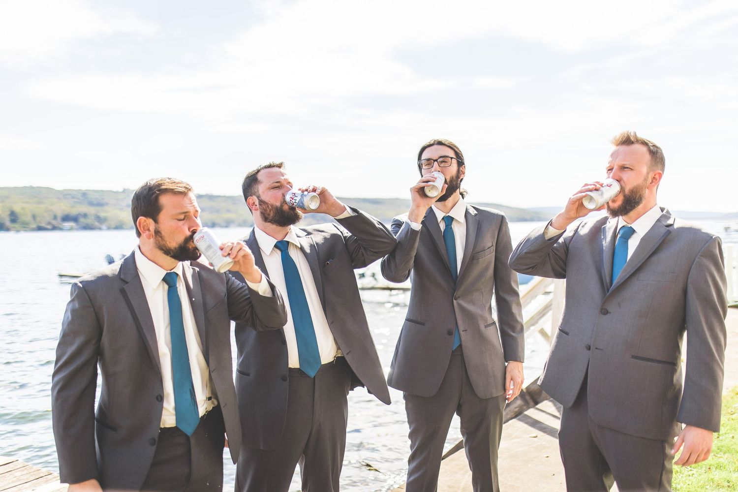 Wedding party in gray suits and blue ties pose together by the water.