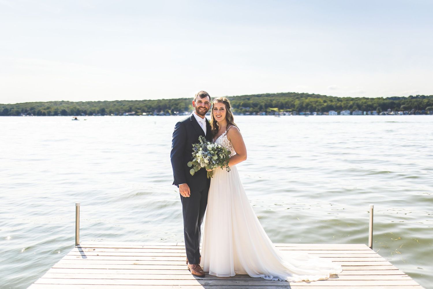 Newlyweds pose together on wooden dock overlooking serene lake.