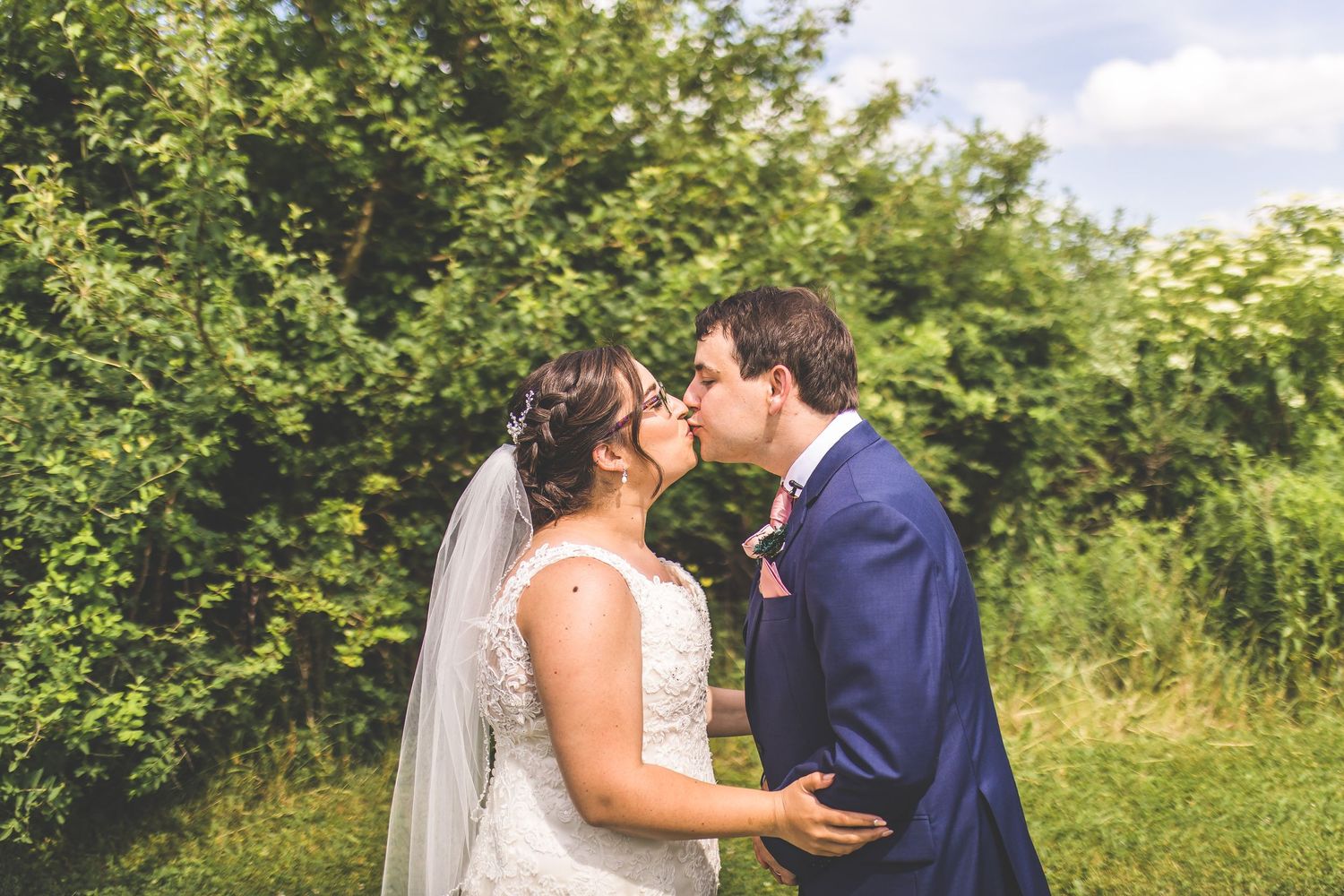 A couple shares romantic moments in a sunny outdoor garden setting wearing wedding attire.