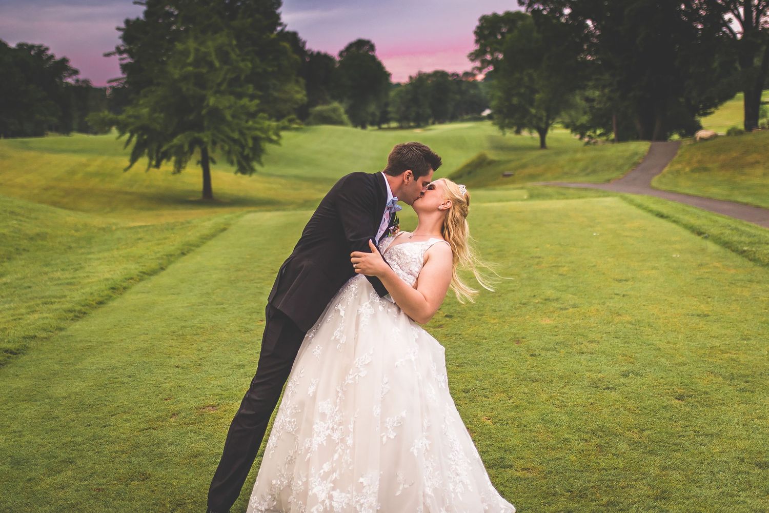 Wedding couple dances playfully on a scenic golf course during golden hour.