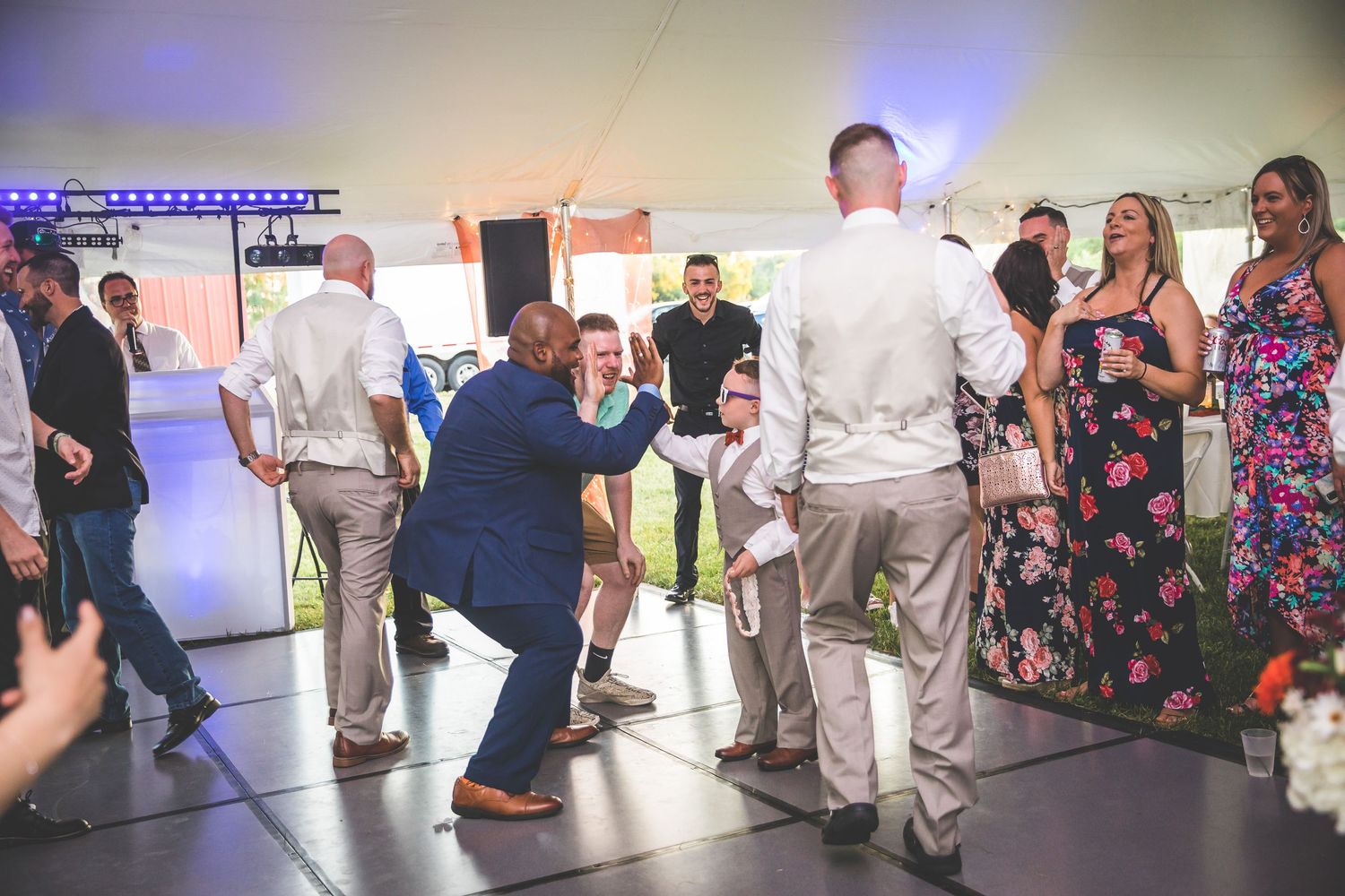 Wedding reception guests dancing in a spacious venue with blue accent lighting.