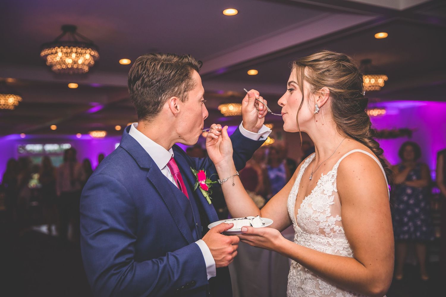 Wedding couple shares cake cutting moment at reception with purple uplighting.