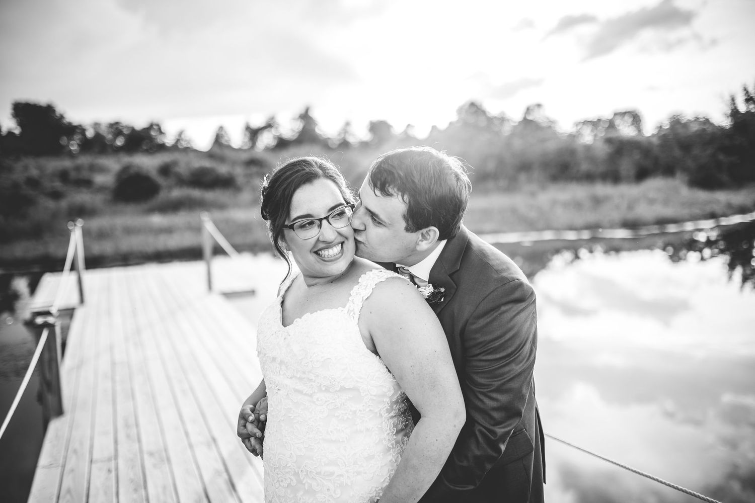 Black and white wedding portraits captured on a lakeside dock at sunset.