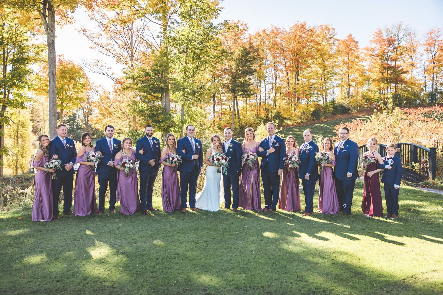 Wedding party in purple dresses posed outdoors during fall season.