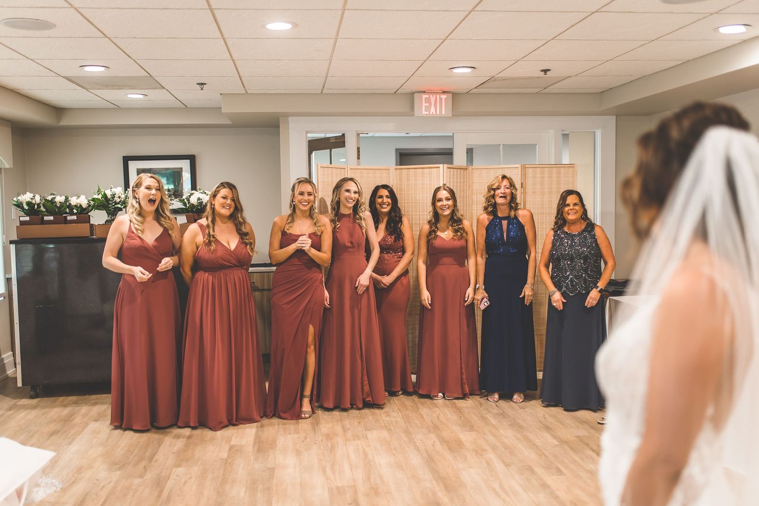 Wedding party in burgundy dresses gathered in an indoor venue.
