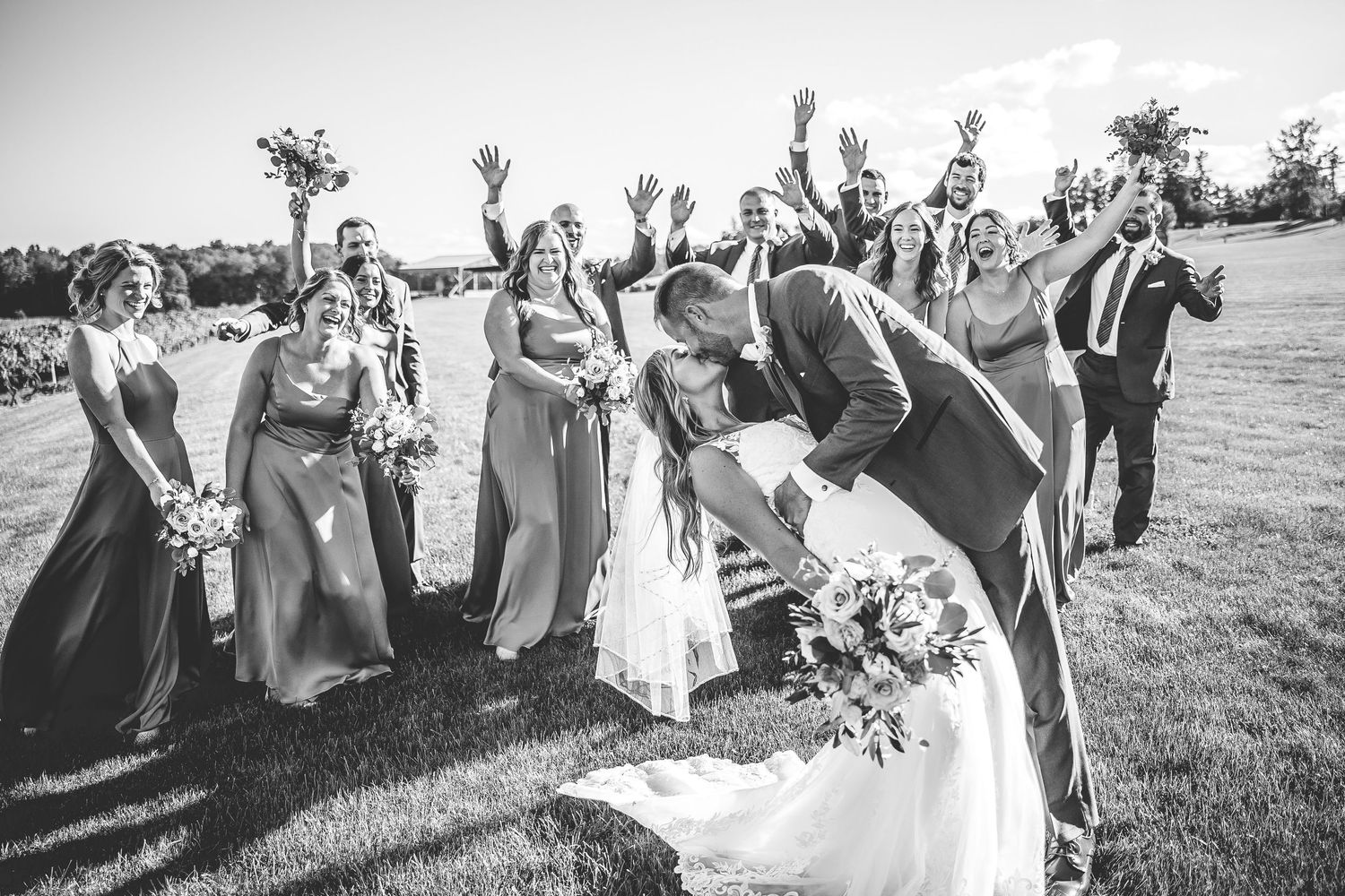 Black and white photo of a wedding party laughing together outdoors during a candid moment.