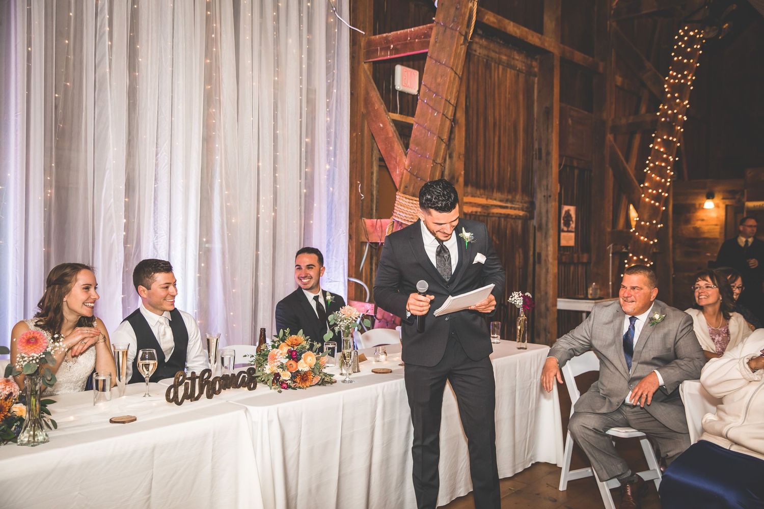 Wedding reception setup in a rustic barn with elegant white draping and table settings.