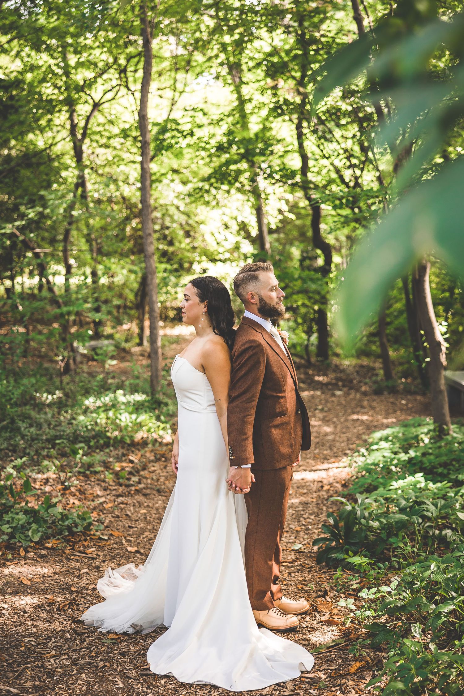 Wedding couple poses together on a winding forest path with beautiful natural lighting.