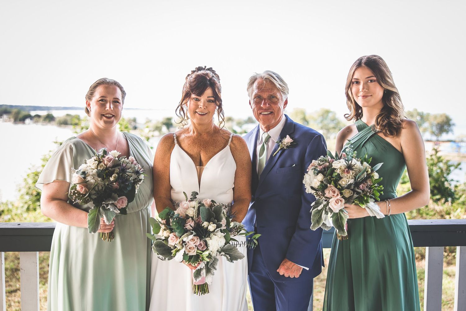 Wedding party members in coordinating blue and green dresses pose with bouquets.