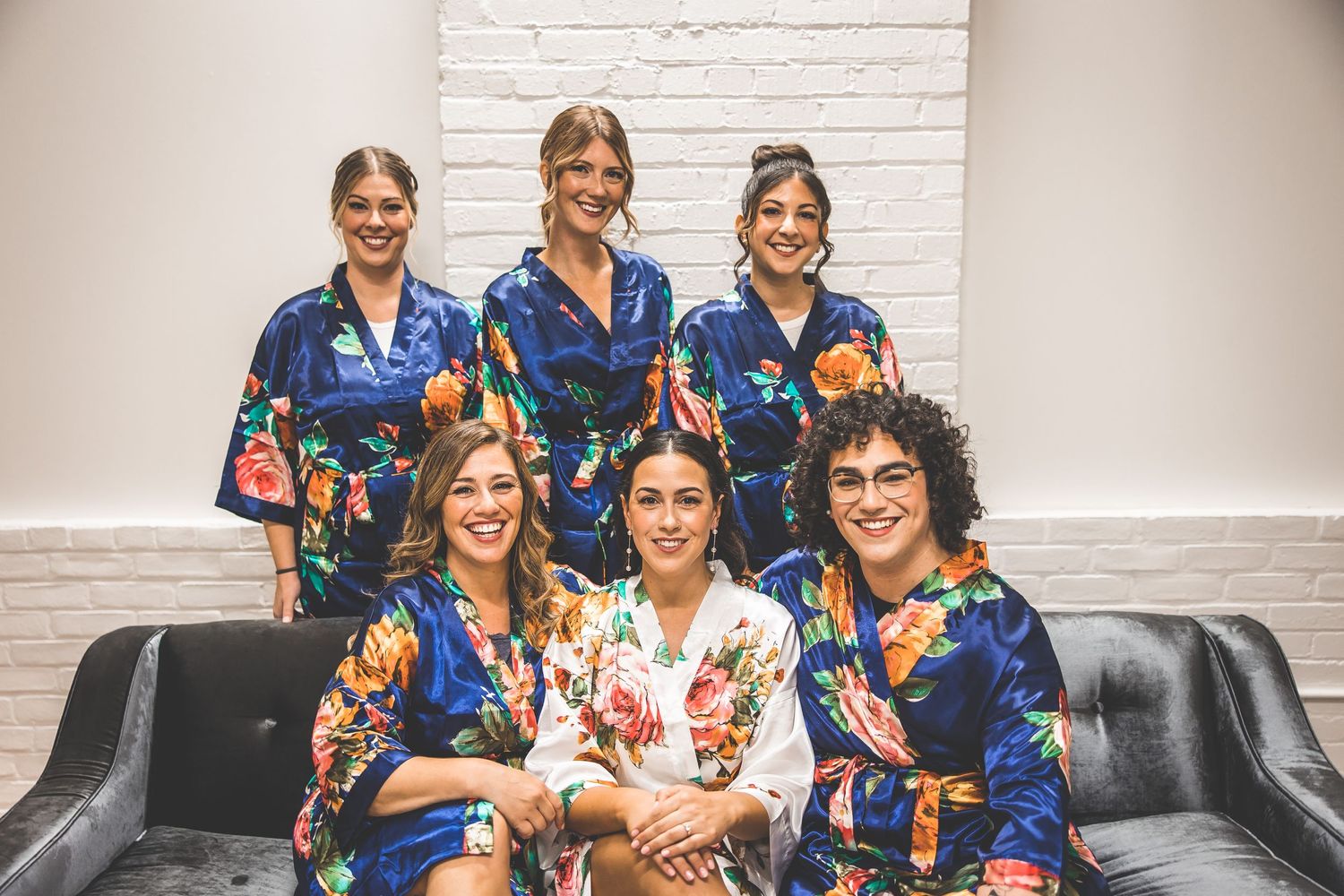 Wedding party in blue floral robes sitting together on grey couch.