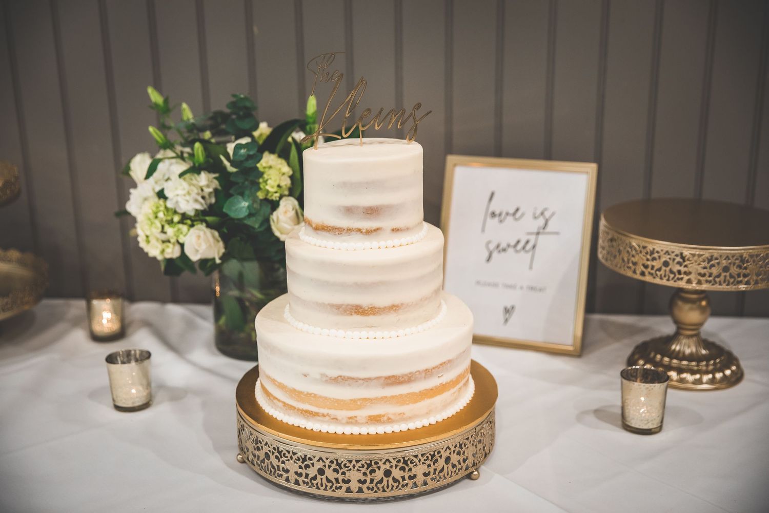 Elegant three-tiered white wedding cake displayed on a gold decorative stand.