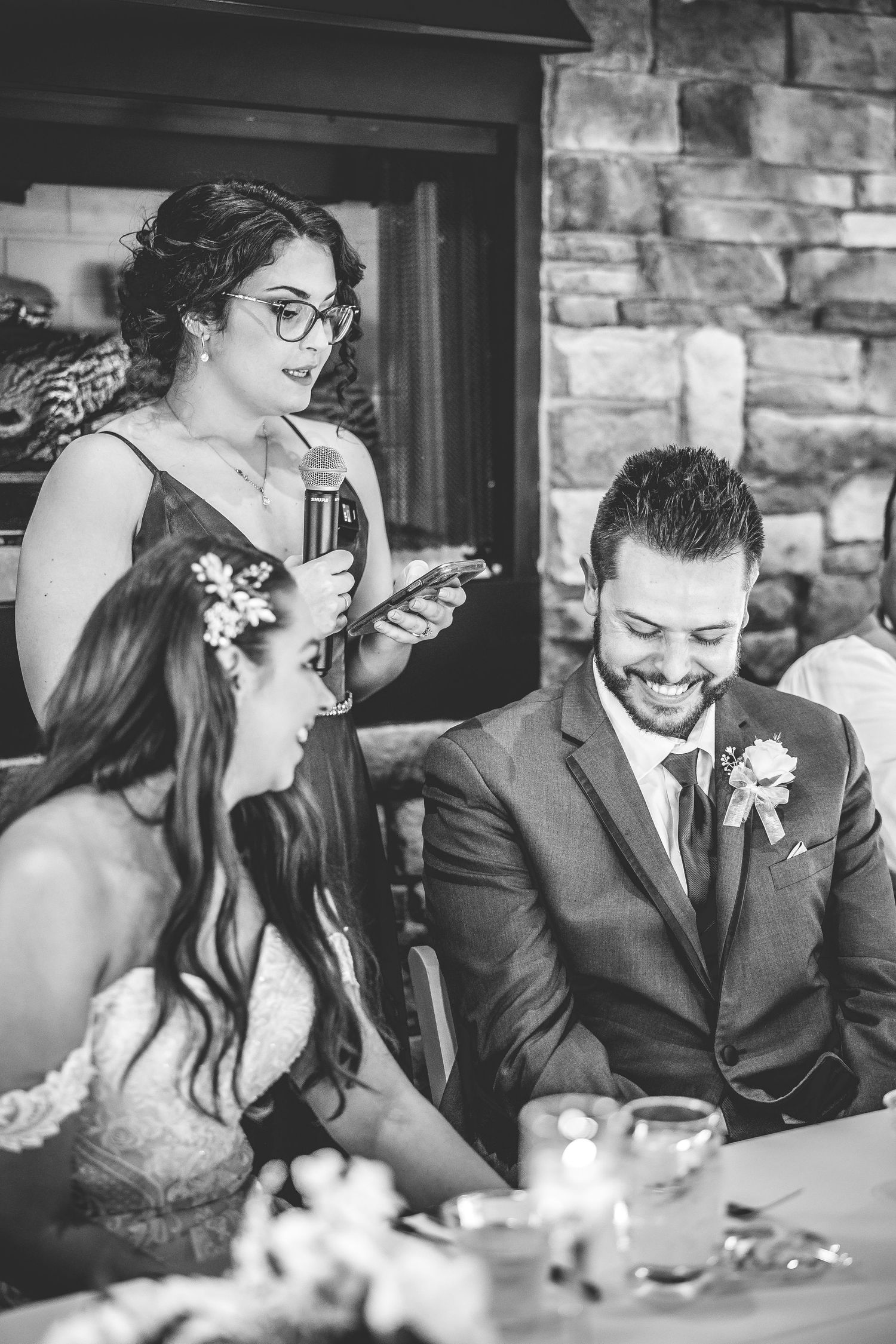 Wedding party members share laughs during reception speeches at head table.